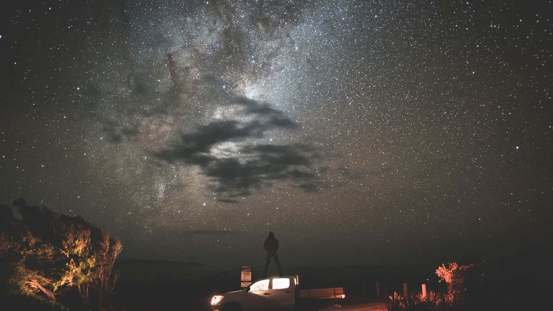 夜空 桌布 壁紙 — 一個孤獨的身影站在卡車頂上，頭頂上是令人嘆為觀止的星空，銀河拱起。