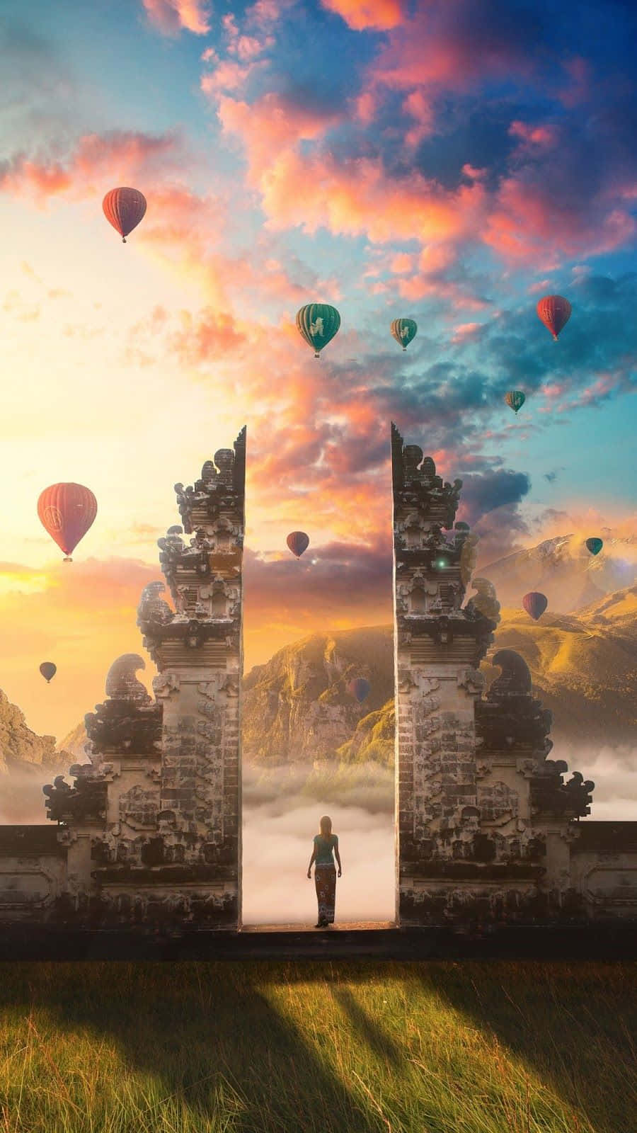 Hot Air Balloon 桌布 壁紙 — 一個孤獨的身影站在古老的石門之間，色彩繽紛的熱氣球在充滿活力的日落天空中飄蕩。