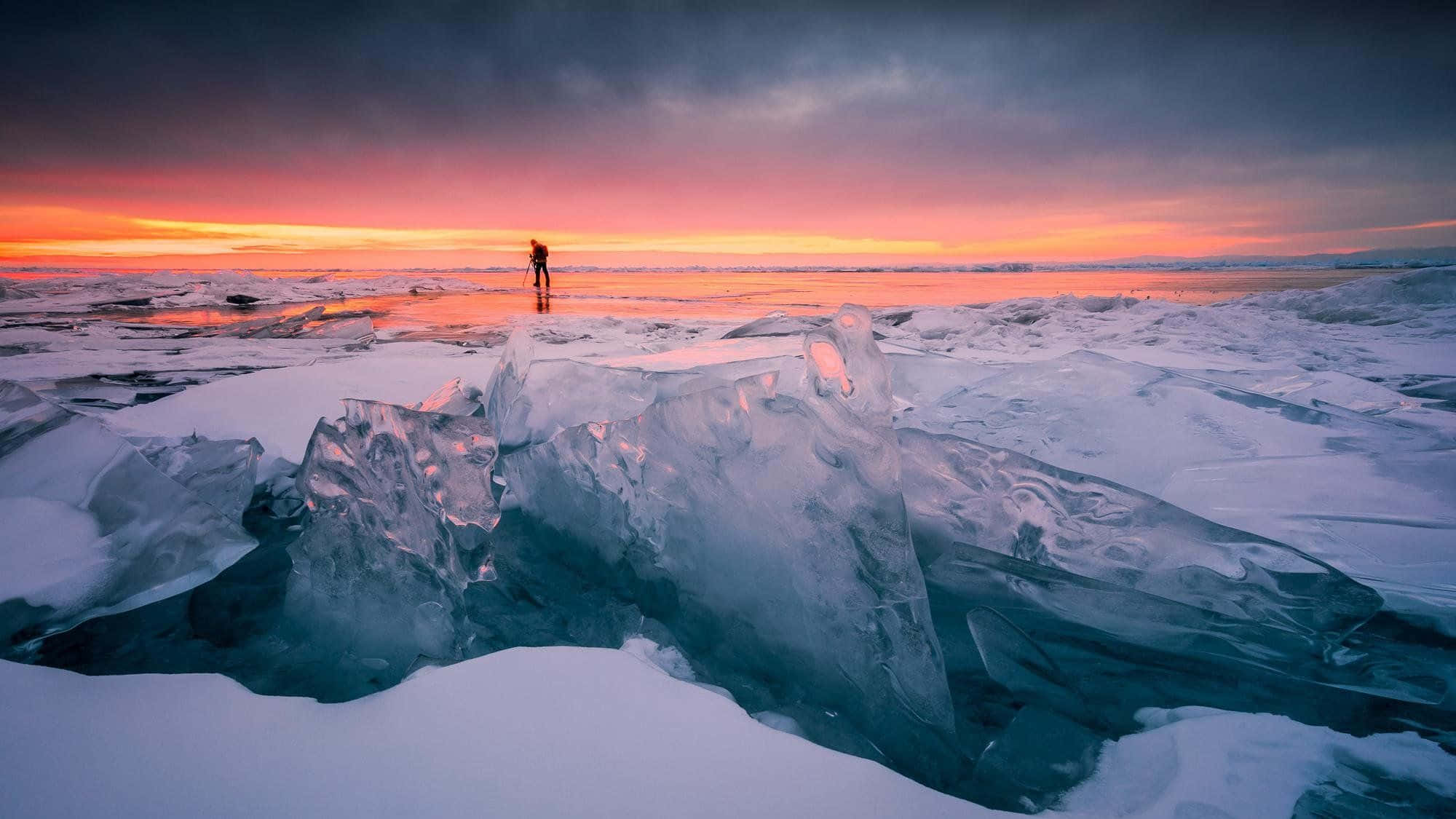 Frozen Lake 桌布 壁紙 — 一個孤獨的身影站在夕陽下的冰凍湖面上，周圍是鋸齒狀的冰層，天空如火般燃燒。