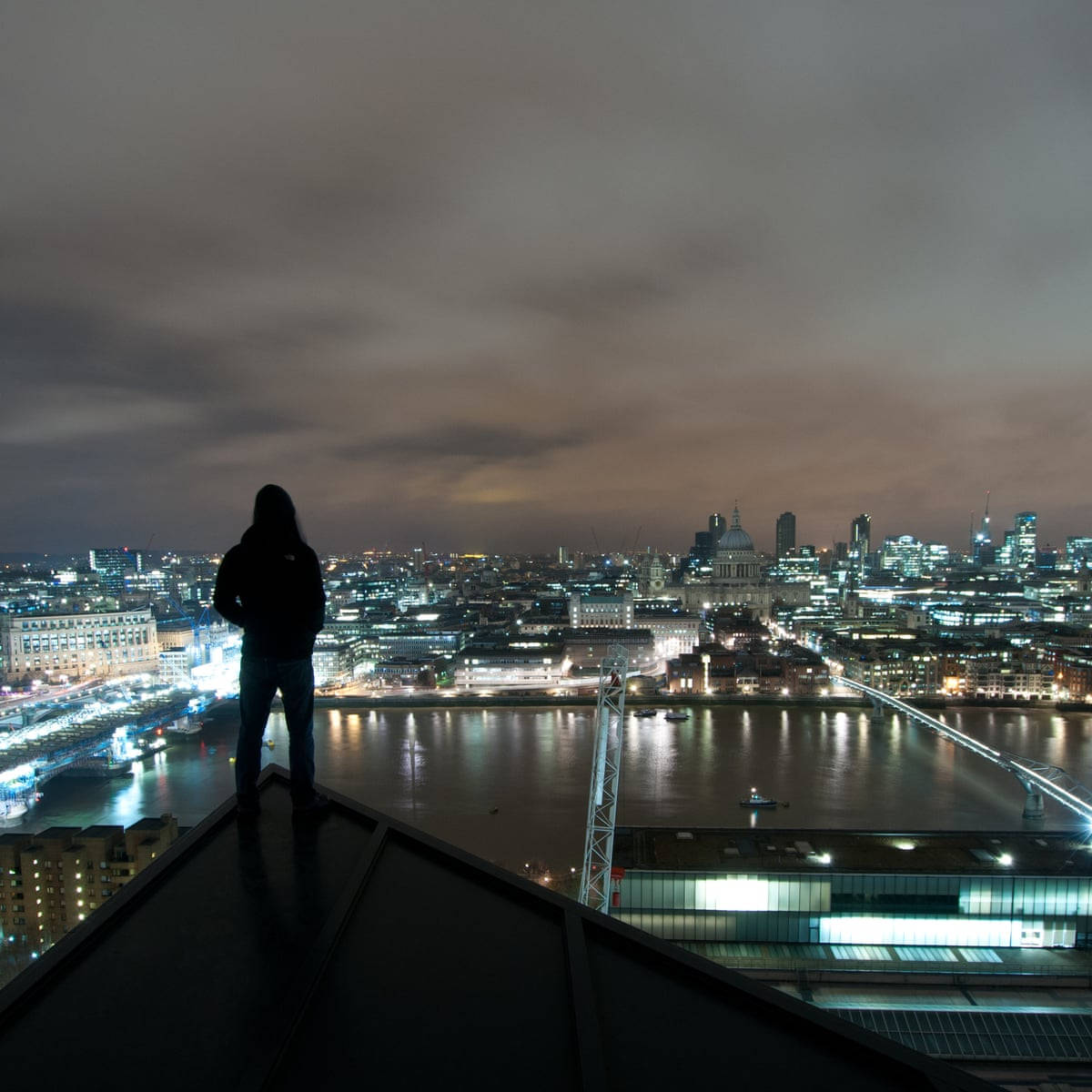 City At Night 桌布 壁紙 — 一個孤獨的身影站在屋頂上，俯瞰夜晚倫敦閃爍的天際線，泰晤士河倒映著城市的燈光。