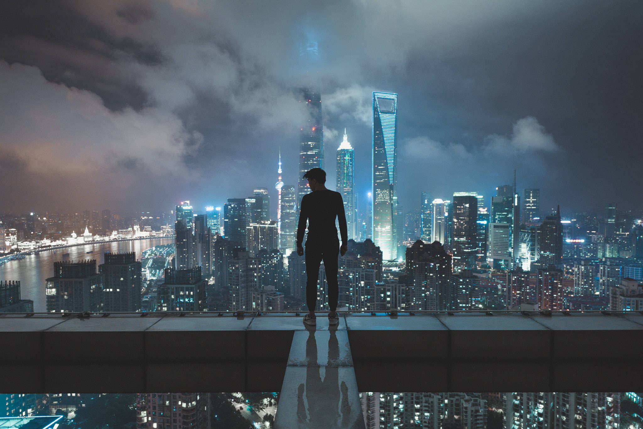 Shanghai 桌布 壁紙 — 一個孤獨的身影站在屋頂上，俯瞰著多雲夜空下霓虹閃爍的廣闊城市景觀。