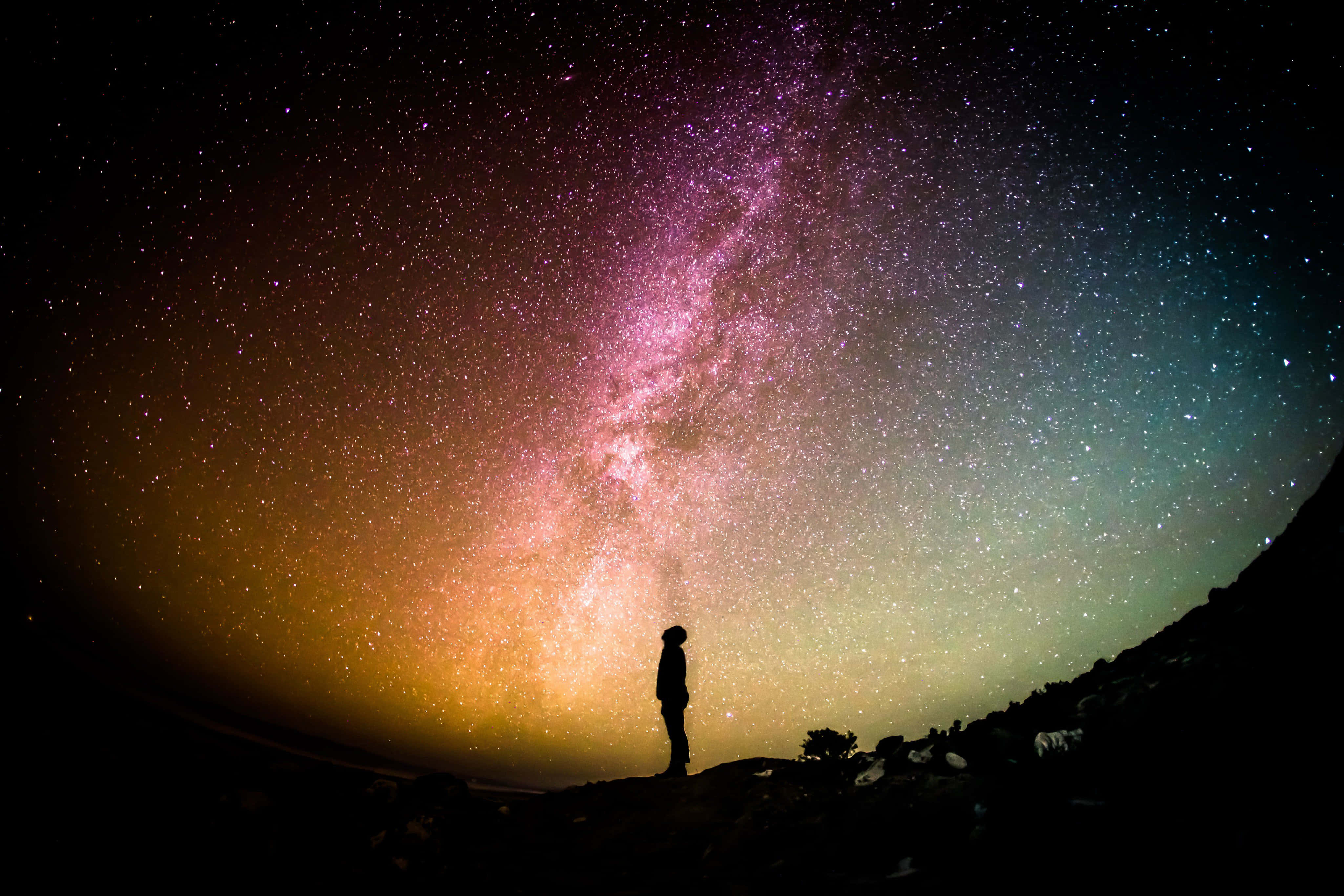 Starry 桌布 壁紙 — 一個孤獨的身影站在山丘上，仰望橫跨繁星夜空、色彩鮮豔的紫金色銀河。