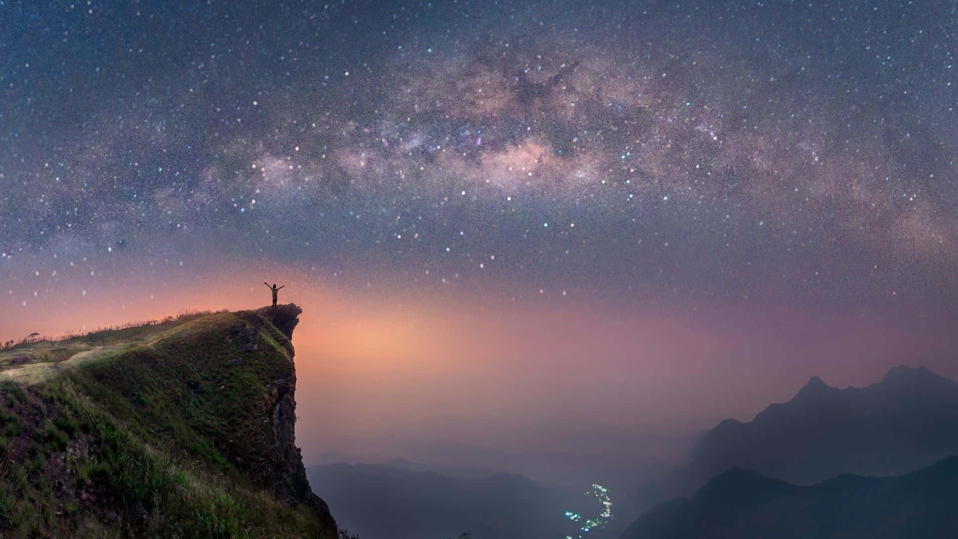 Stars 桌布 壁紙 — 一個孤獨的身影站在山崖上，雙臂高舉，背景是令人驚嘆的銀河系，帶有粉紅色和紫色的暮色色調。