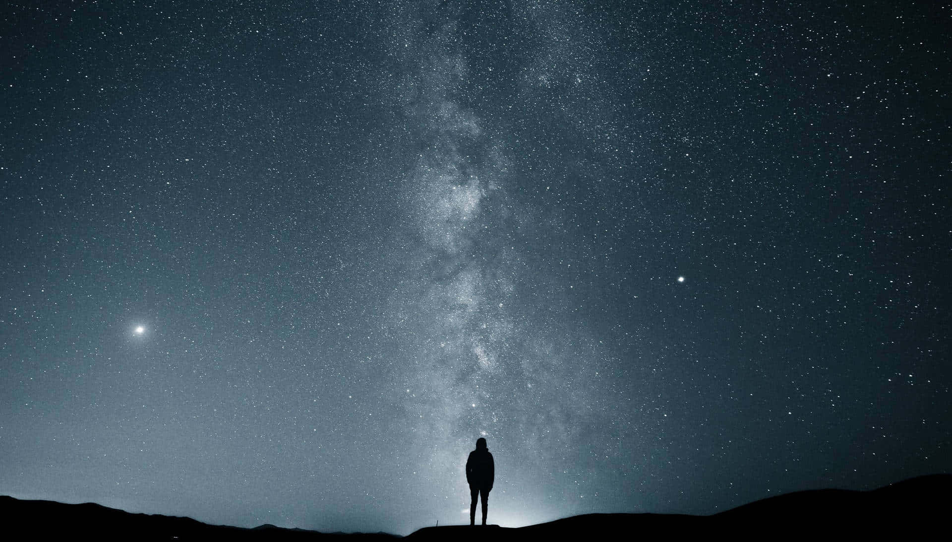 Alone 桌布 壁紙 — 一個孤獨的身影站在山頂上，仰望佈滿銀河和明亮天體的壯麗星空。