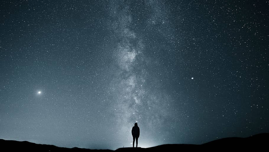 夜空 桌布 壁紙 — 一個孤獨的身影站在山頂上，仰望在繁星點點的夜空中閃耀的銀河系。