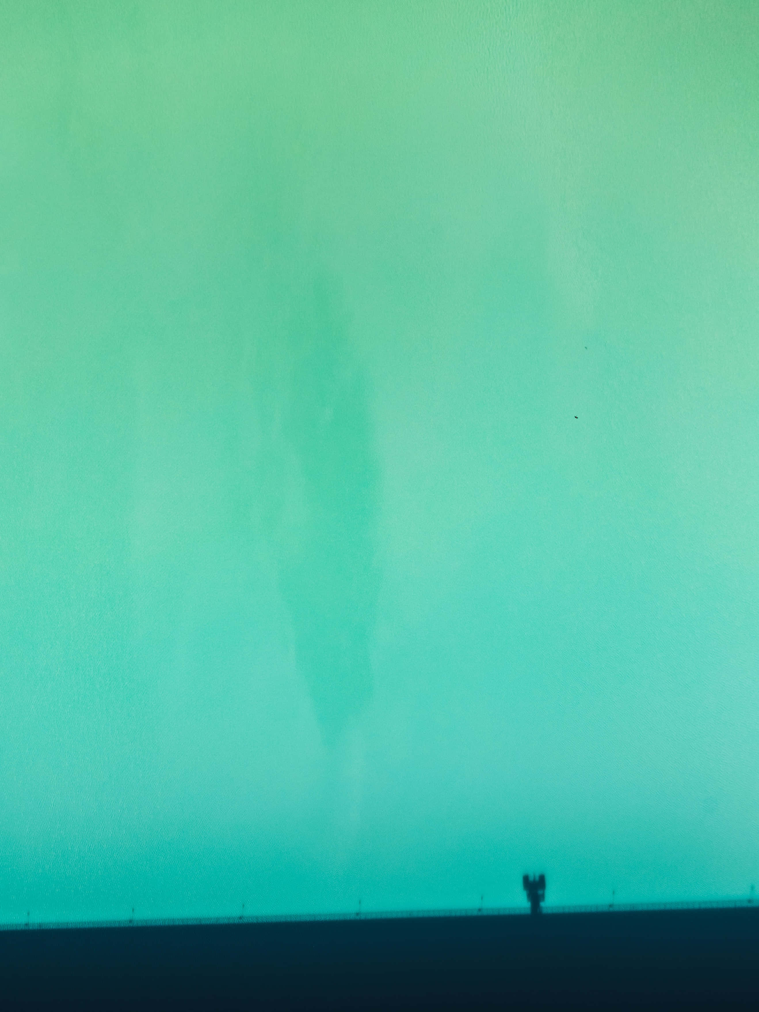 Turquoise Green 桌布 壁紙 — 一個孤獨的身影站在廣闊的綠松色天空前，遠處有微弱的龍捲風在旋轉。