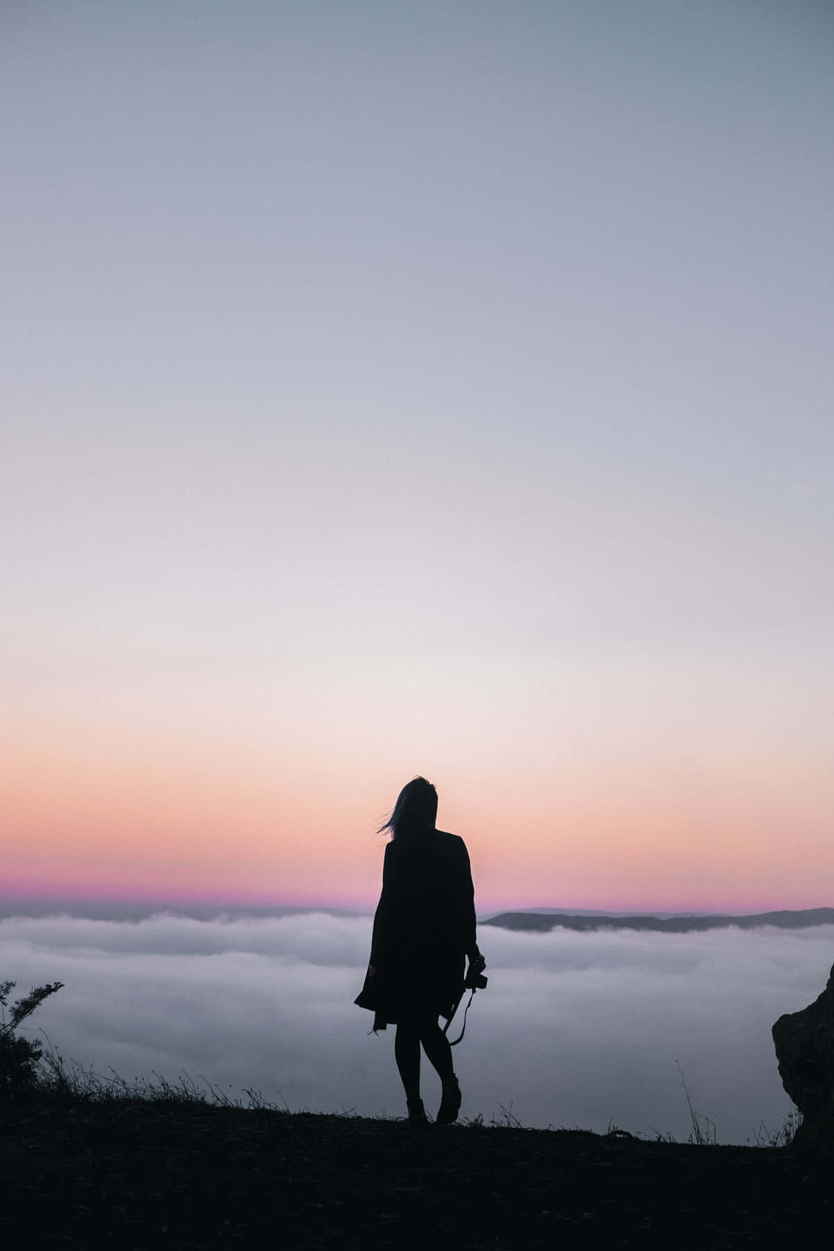 Silhouette 桌布 壁紙 — 一個孤獨的身影站在懸崖頂上，俯瞰著暮色中粉藍漸變的天空下的雲海。