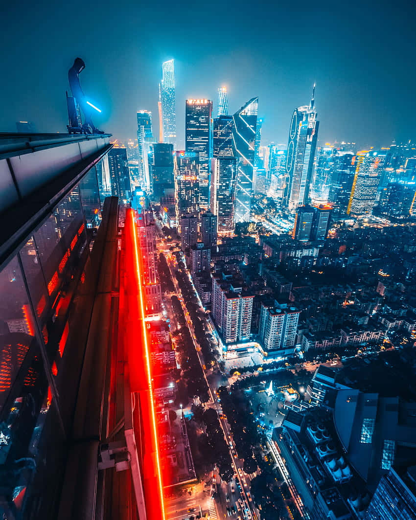 Rooftop 桌布 壁紙 — 一個孤獨的身影站在摩天大樓的邊緣，俯瞰著夜晚充滿活力的霓虹燈城市景觀，下方有發光的塔樓和一條引人注目的紅色光跡。