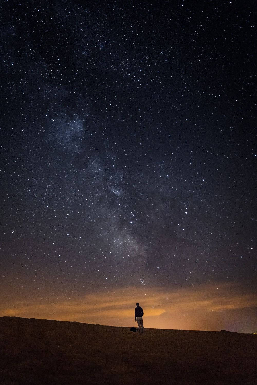 夜空 桌布 壁紙 — 一個孤獨的身影站在沙漠沙丘上，仰望充滿銀河和流星的壯麗星空。