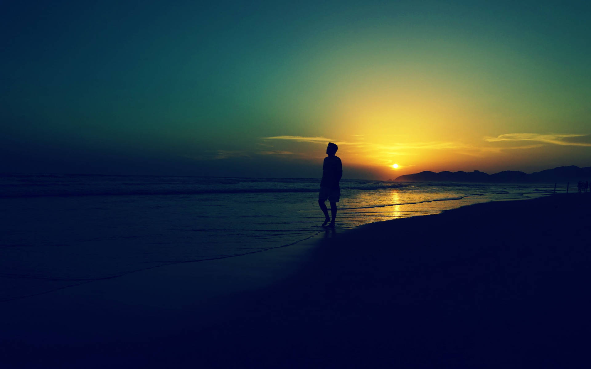Alone 桌布 壁紙 — 一個孤獨的身影站在沙灘上，看著夕陽落在遠山之上，在水面上灑下金色的光芒。