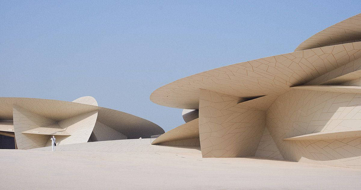 Qatar 桌布 壁紙 — 一個孤獨的身影站在流暢的米色建築曲線前，背景是清澈的藍天。