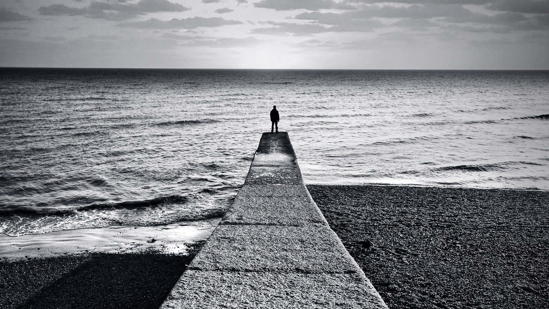 Lonely 桌布 壁紙 — 一個孤獨的身影站在混凝土碼頭的盡頭，碼頭在陰天延伸至廣闊的海洋。