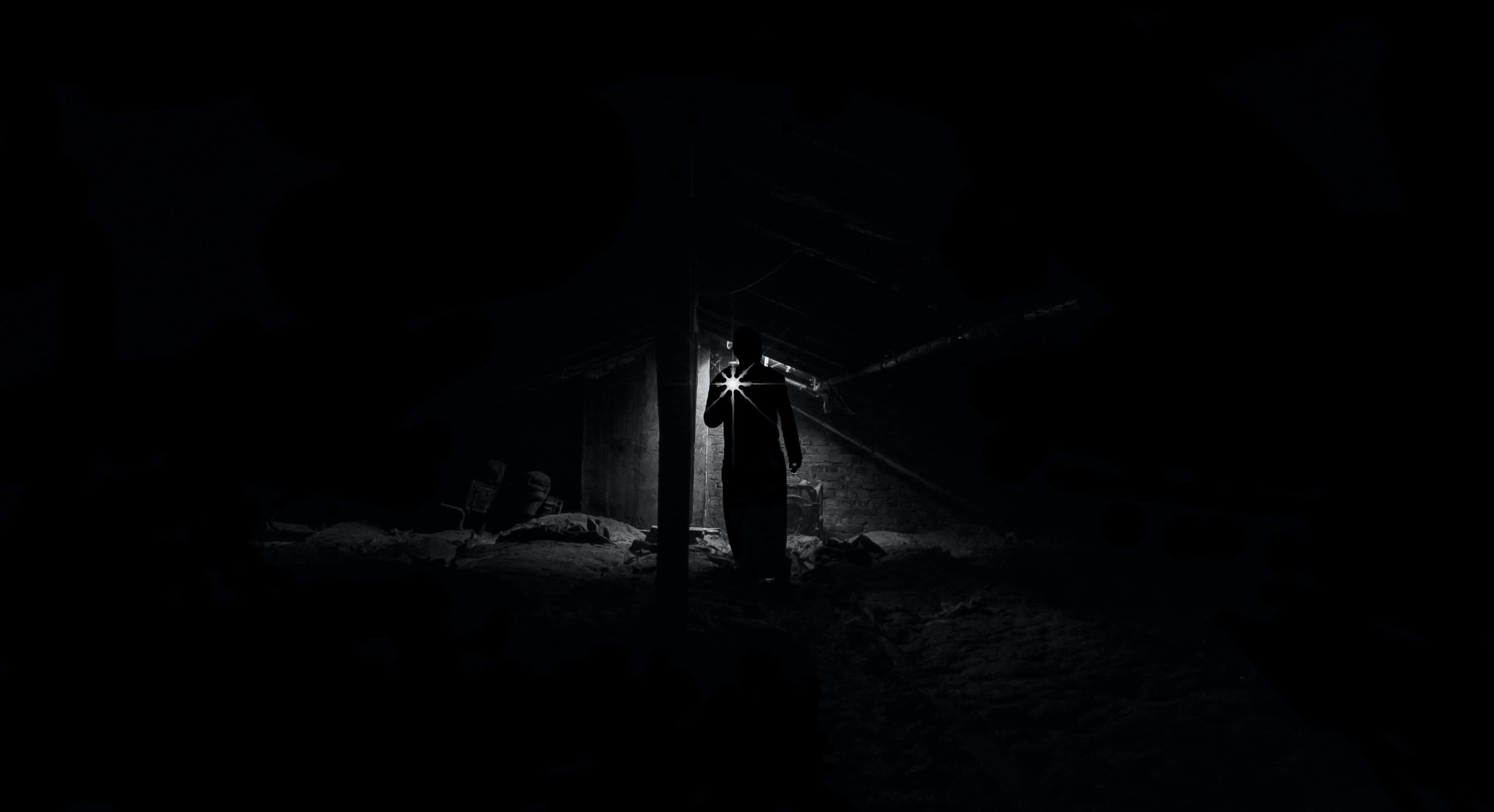 Dark Fear 桌布 壁紙 — 一個孤獨的身影站在漆黑的廢墟中，手持手電筒劃破黑暗，照亮灰塵和瓦礫。