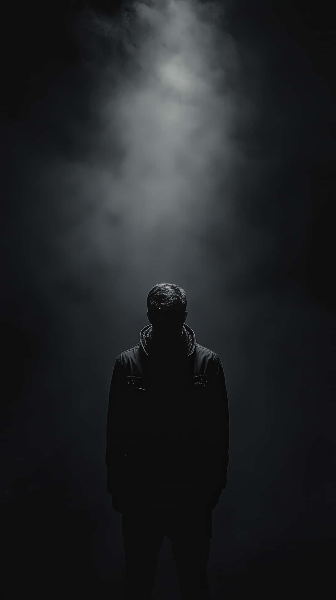 Mysterious silhouette of a hooded man standing in dramatic fog and darkness 壁紙 — 一個孤獨的身影站在陰影中，一束光線穿透濃煙照射而下。