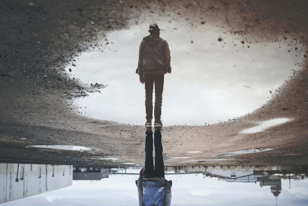 reflection 桌布 壁紙 — 一個孤獨的身影站在雨水坑中，倒影映照在下方，周圍是濕漉漉的瀝青和城市衰敗。