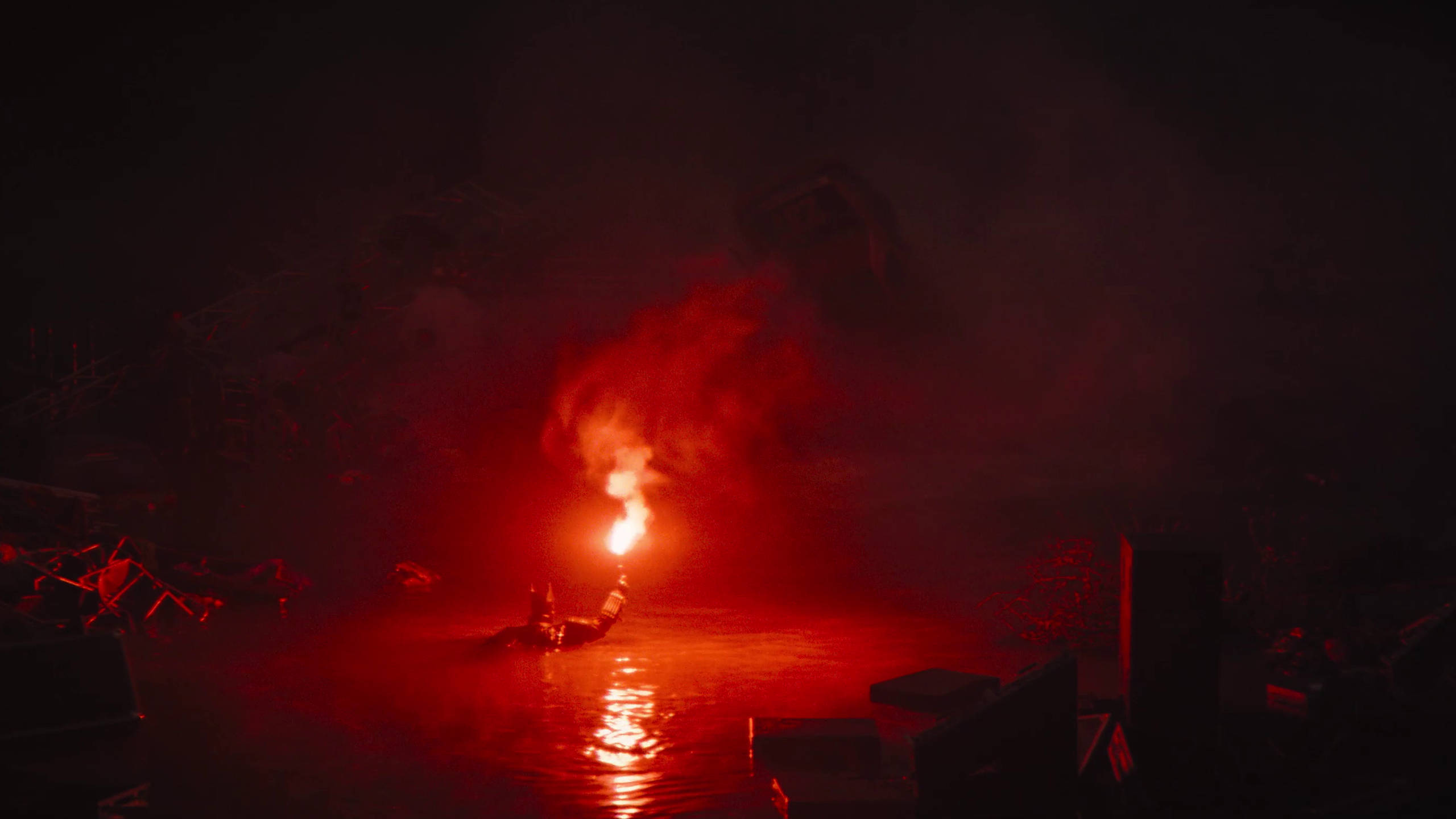 2560 X 1440 Movie 桌布 壁紙 — 一個孤獨的身影站在黑暗的水中，手持燃燒的火把，在煙霧和碎片上投射出詭異的紅光。
