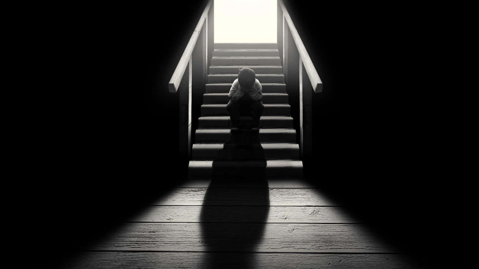 Alone 桌布 壁紙 — 一個孤獨的身影蜷縮在樓梯底部，被上方刺眼的光線照亮，在木地板上投下長長的影子。