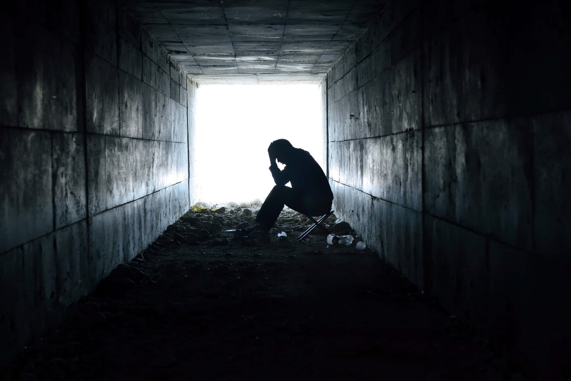 Alone 桌布 壁紙 — 一個孤獨的身影蜷縮在絕望中，坐在黑暗混凝土隧道的盡頭，被出口刺眼的光芒照亮。