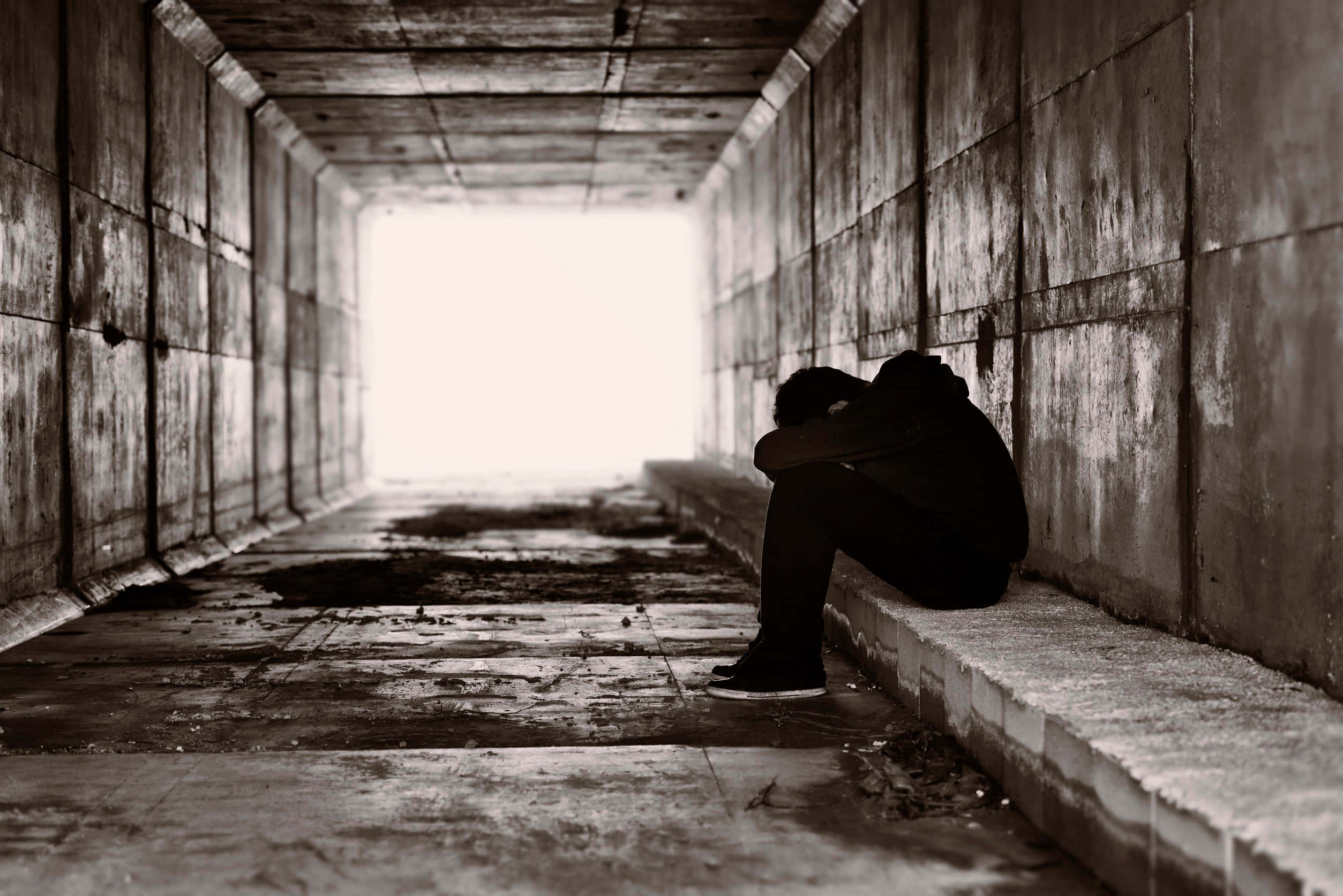 grief 桌布 壁紙 — 一個孤獨的身影蜷縮在絕望中，身處昏暗的混凝土隧道，遠處出口有刺眼的白光照亮。