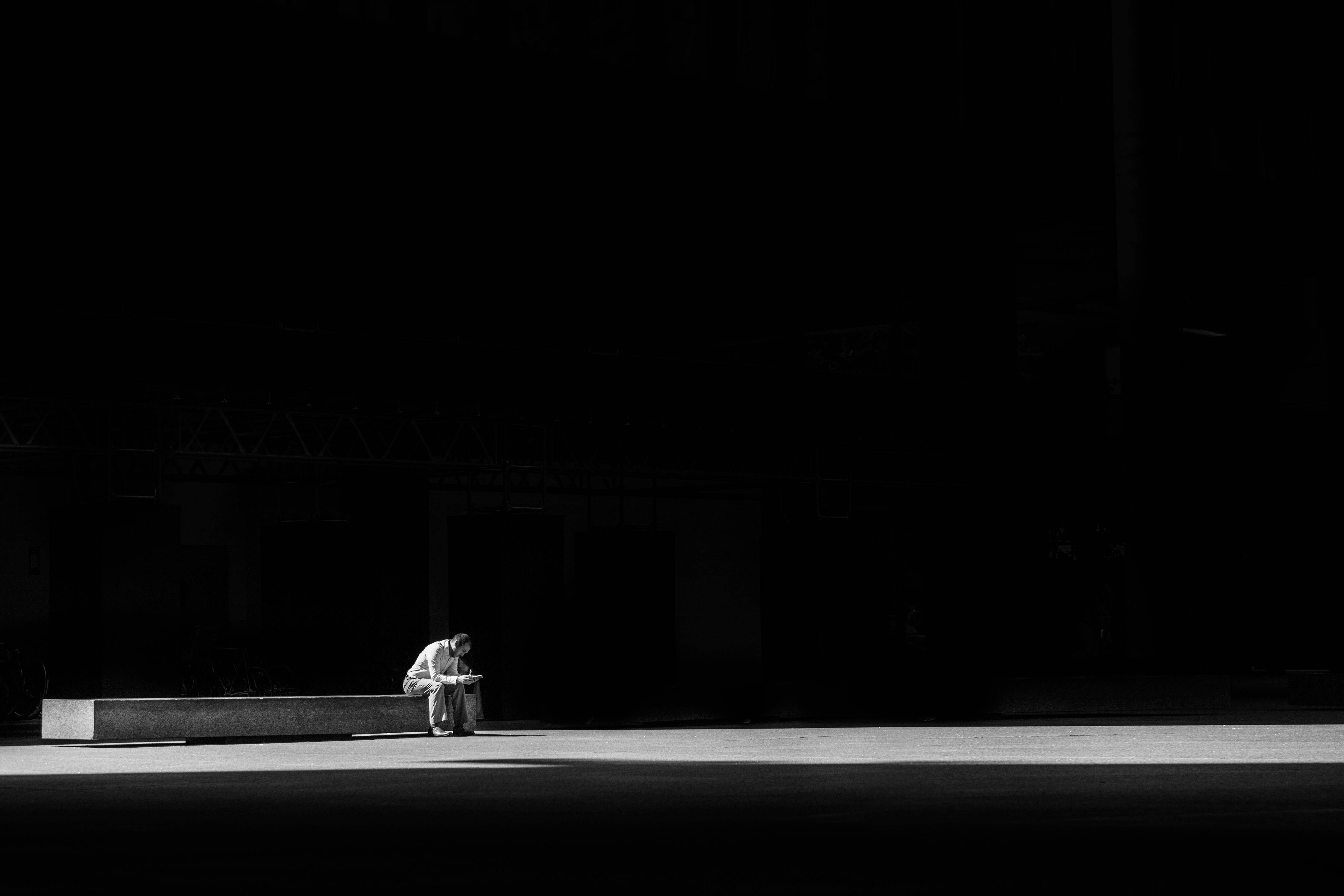 Depression Aesthetic 桌布 壁紙 — 一個孤獨的身影蜷縮在長椅上，身處強烈照明的城市虛空，被深邃的陰影包圍。
