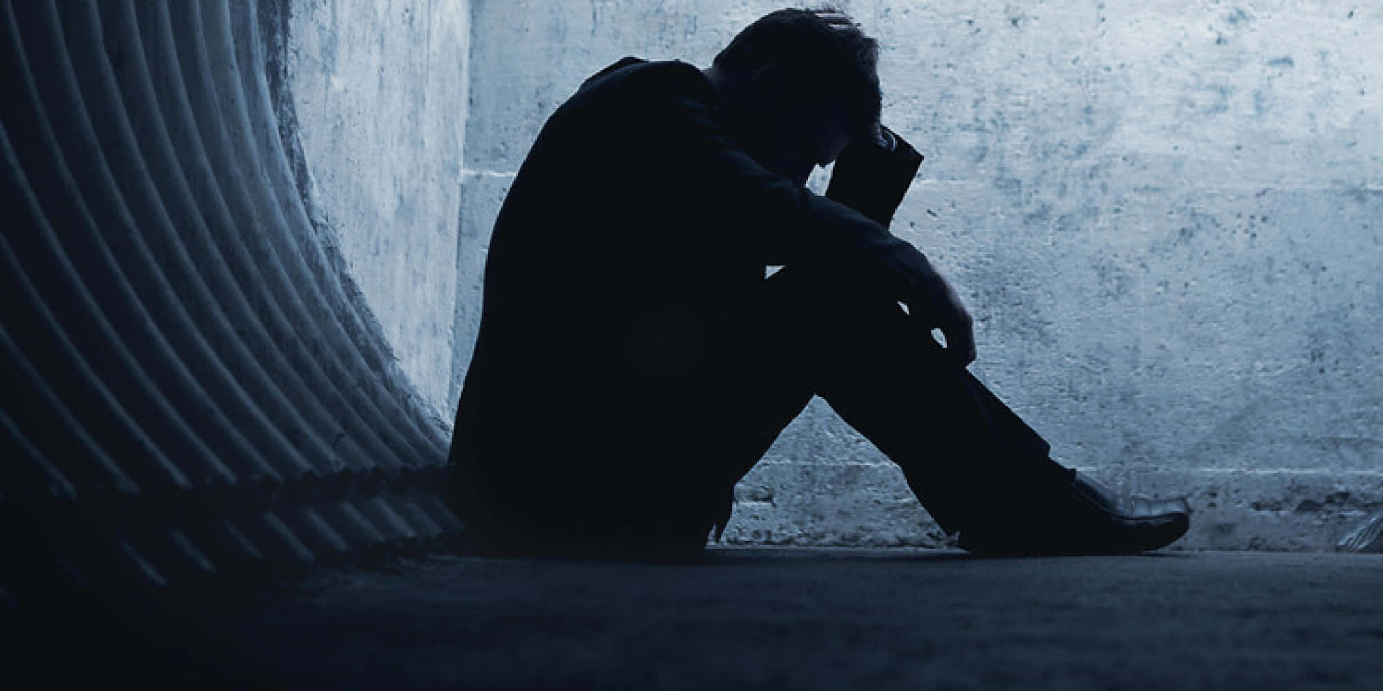 Depressing Profile 桌布 壁紙 — 一個孤獨的身影蜷縮在陰影中，身處冰冷的混凝土隧道內，低垂著頭，陷入無聲的絕望。