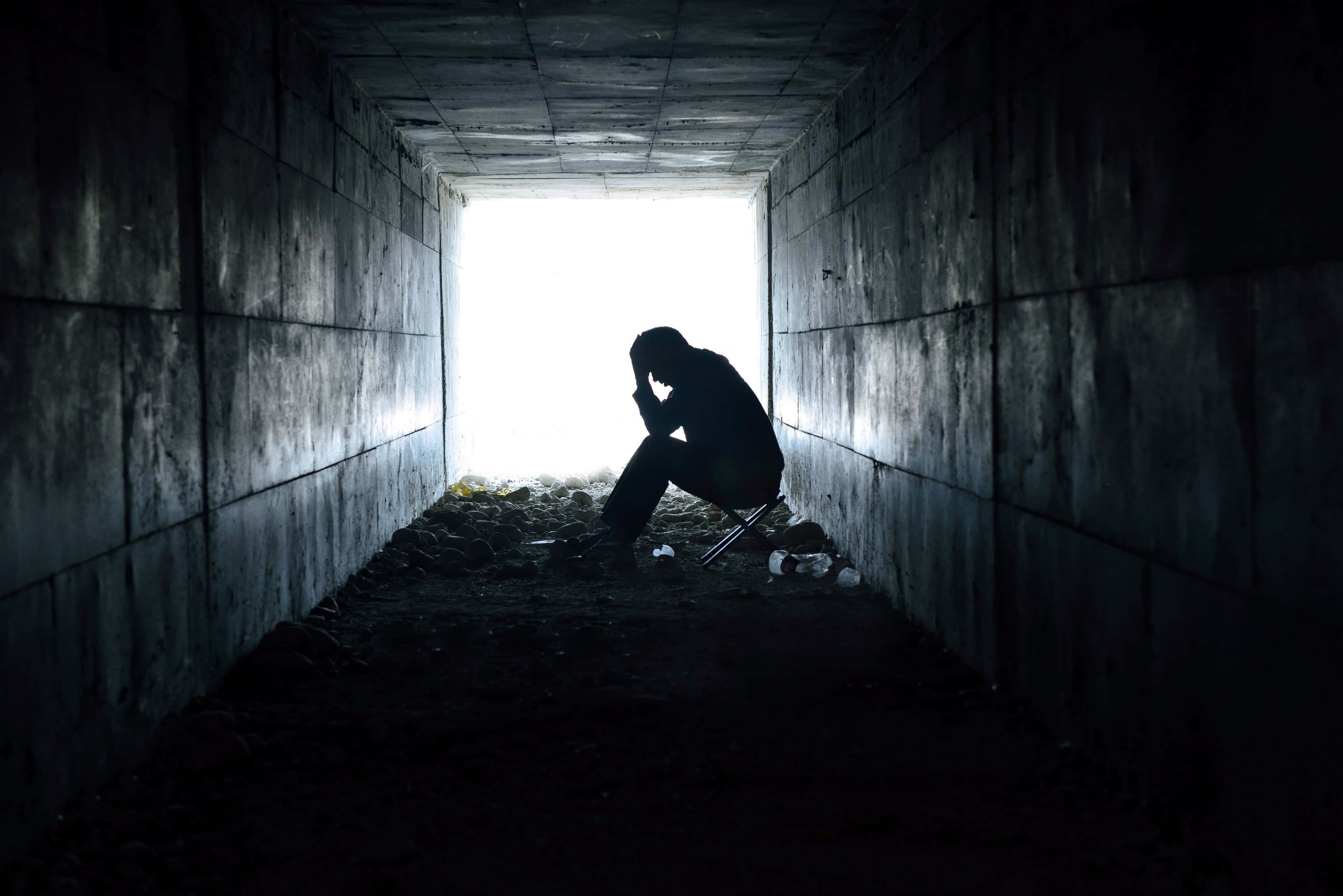 Depressing 桌布 壁紙 — 一個孤獨的身影蜷縮在黑暗的混凝土隧道中，在明亮的出口襯托下形成剪影，傳達出深深的絕望。