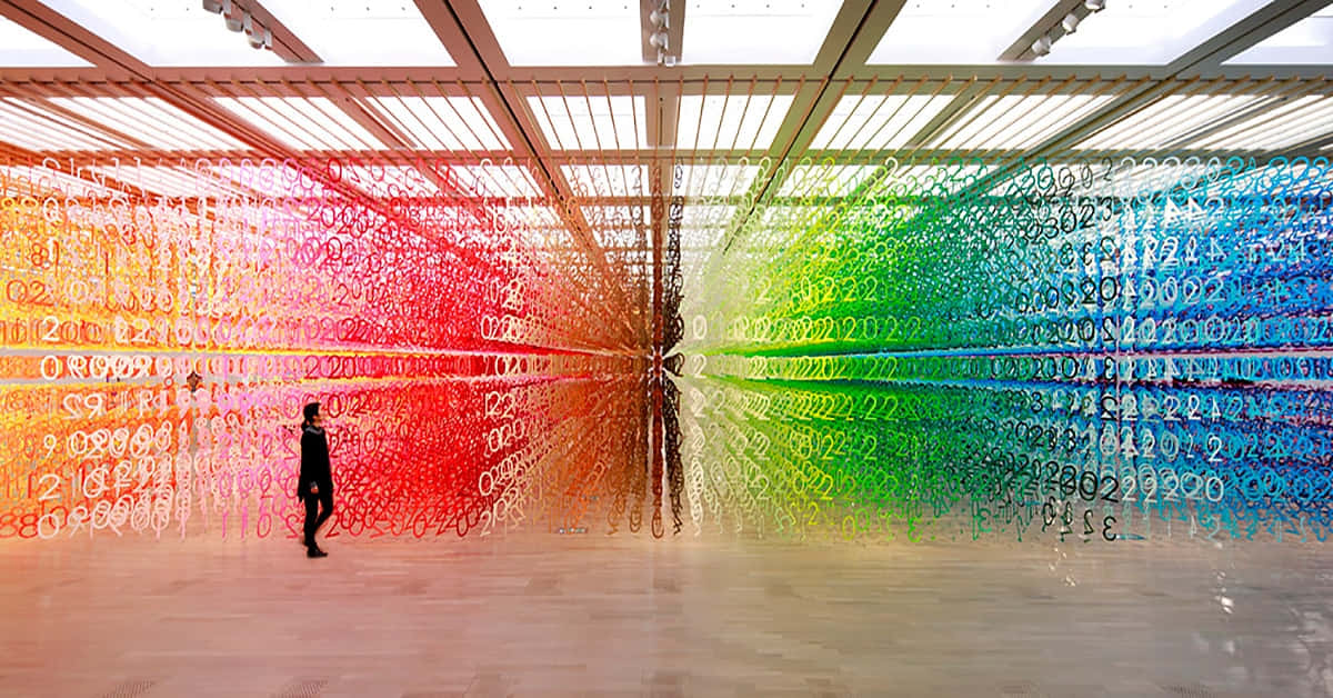 Installation Art 桌布 壁紙 — 一個孤獨的身影走過一個巨大的室內裝置，裝置中懸掛著從網格天花板上垂下的彩虹色數字串。