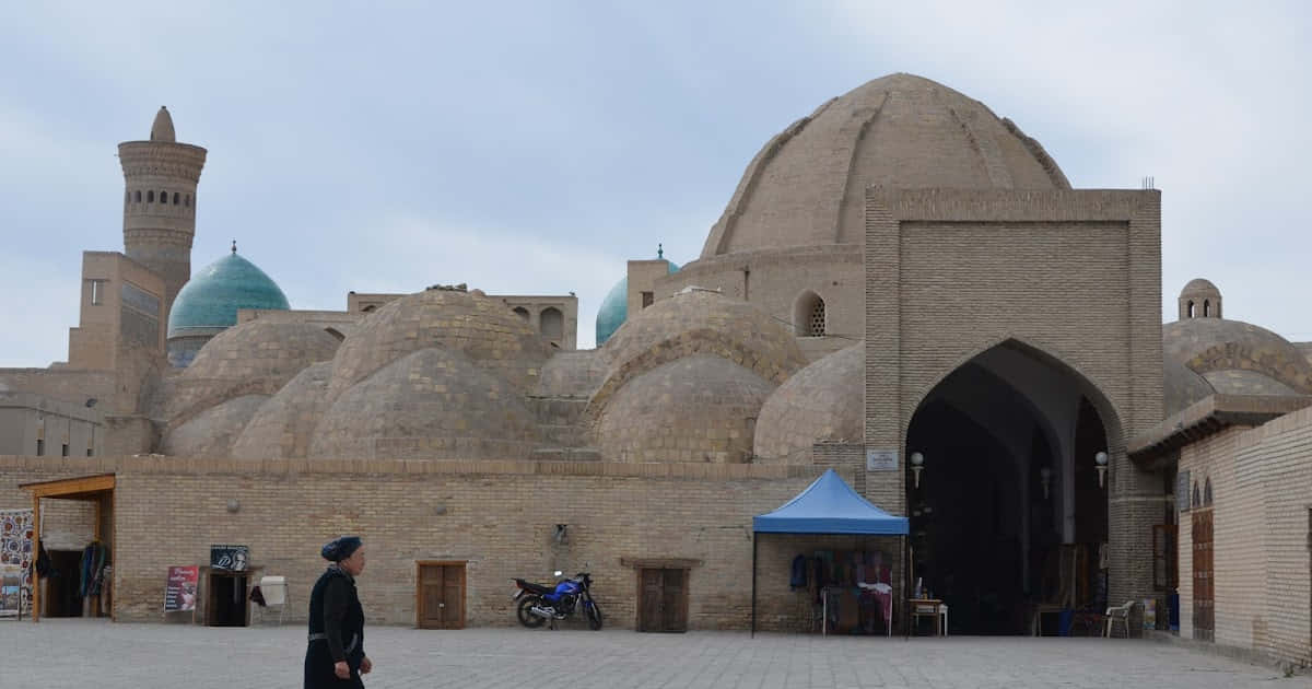 Uzbekistan 桌布 壁紙 — 一個孤獨的身影走過歷史伊斯蘭建築群的古老磚砌圓頂和宣禮塔，天空多雲。