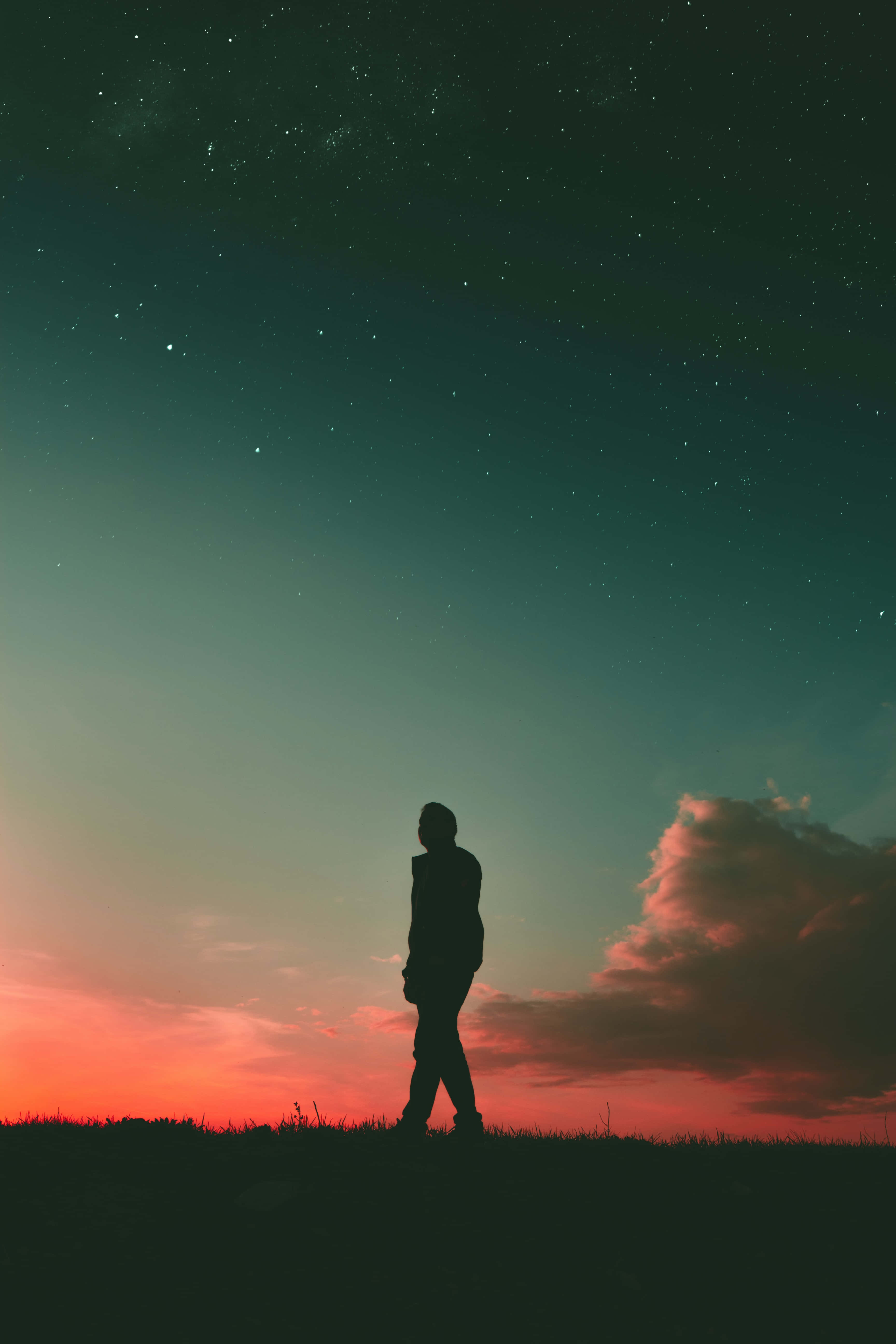 Silhouette 桌布 壁紙 — 一個孤獨的身影走過長滿草的丘陵，天空是星光閃爍的暮色，塗上了青綠色和火橙色的漸變。