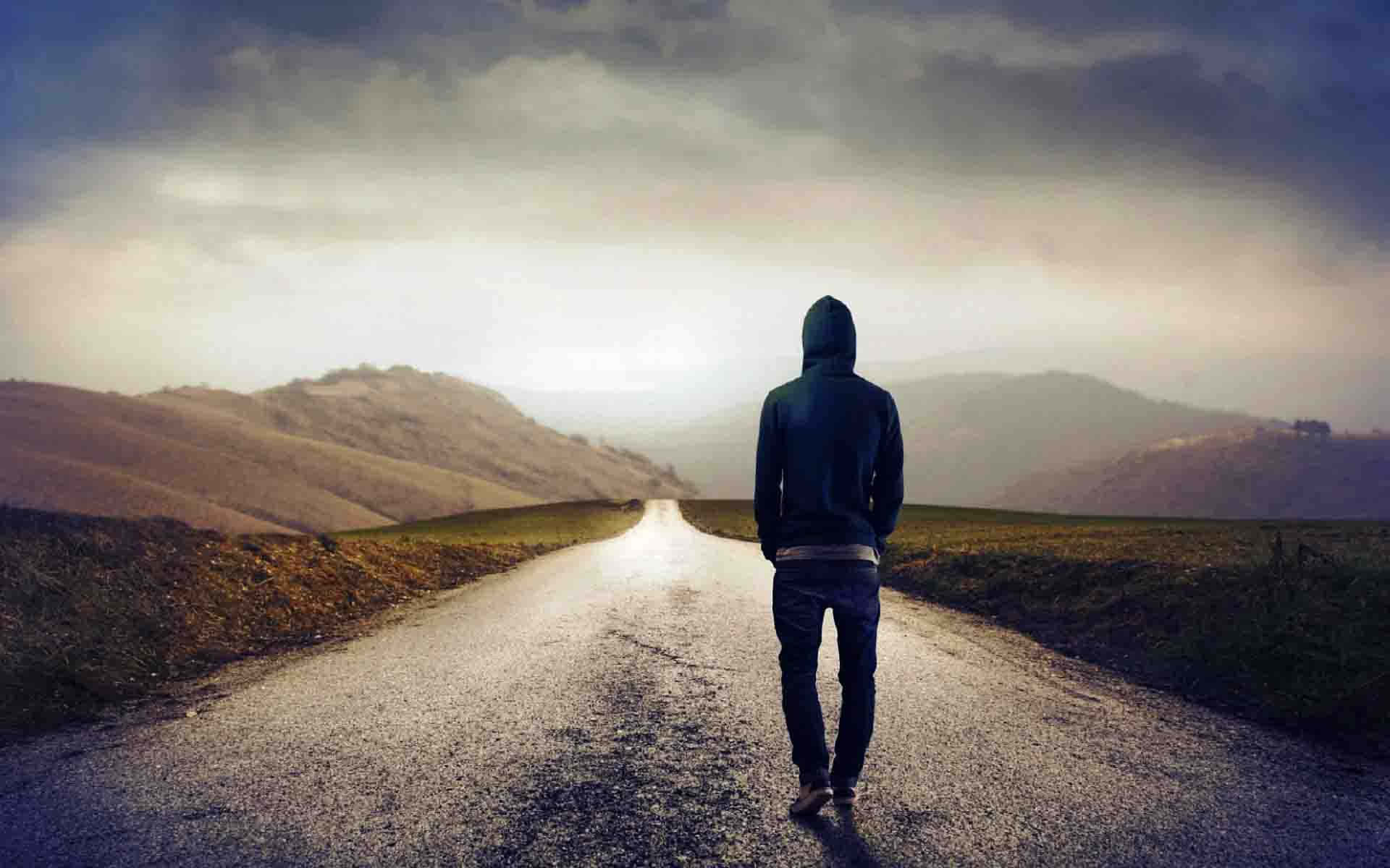 山景 桌布 壁紙 — 一個孤獨的連帽身影沿著霧氣瀰漫的鄉村道路，在陰沉多雲的天空下走向遠方的山丘。