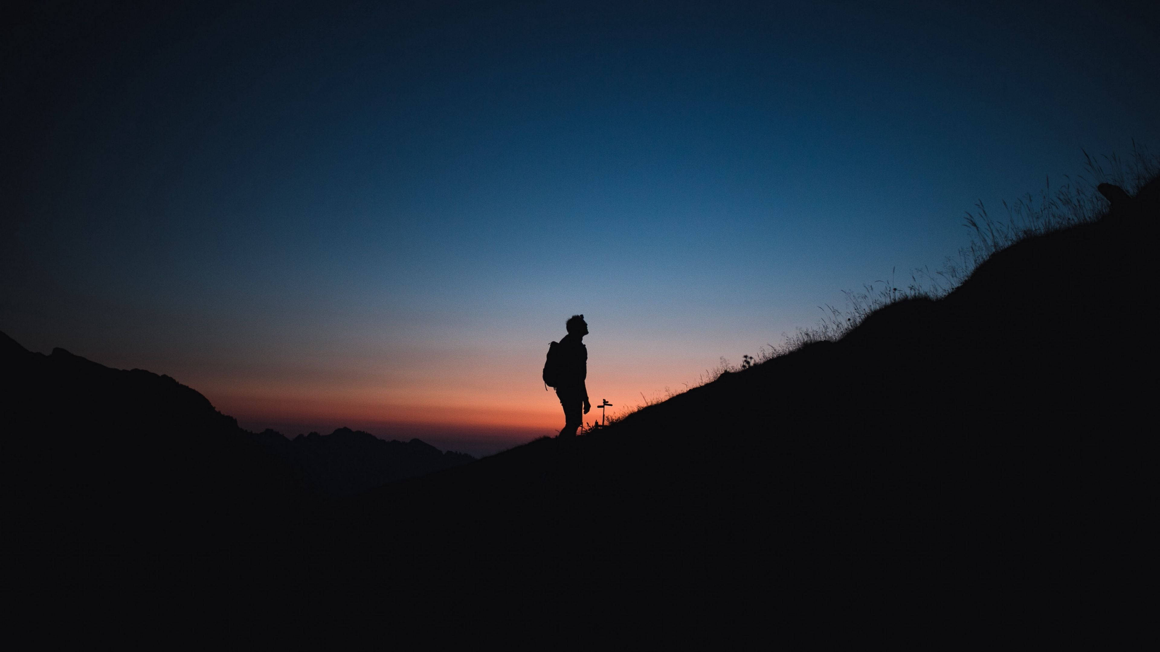 Silhouette 桌布 壁紙 — 一個孤獨的遠足者的剪影站在暮色中的山脊上，背景是深藍和暖橙色的漸變天空。