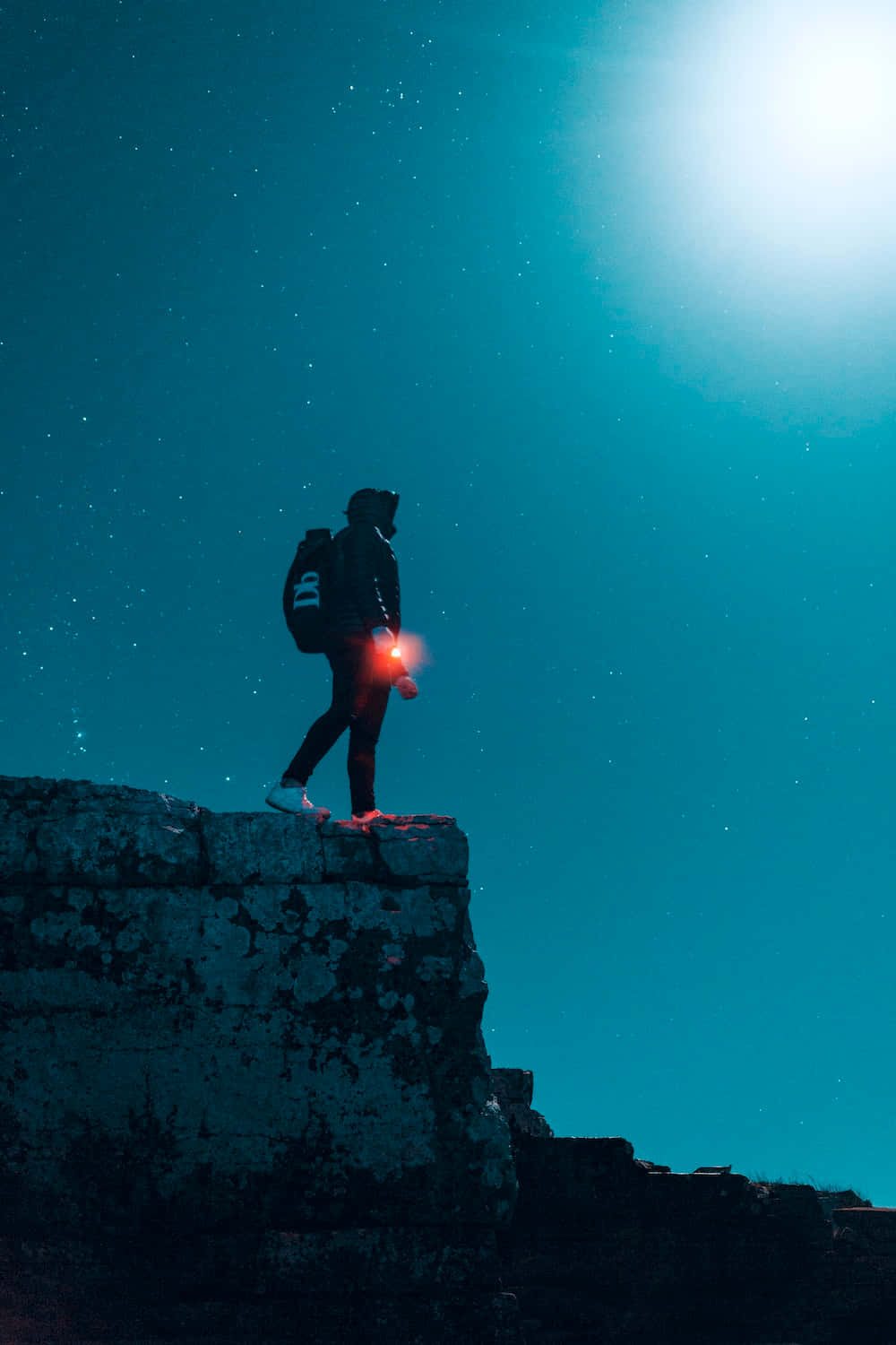 adventure 桌布 壁紙 — 一個孤獨的遠足者站在岩石懸崖頂上，在繁星點點的藍綠色夜空下，手持一個發光的紅色燈籠。