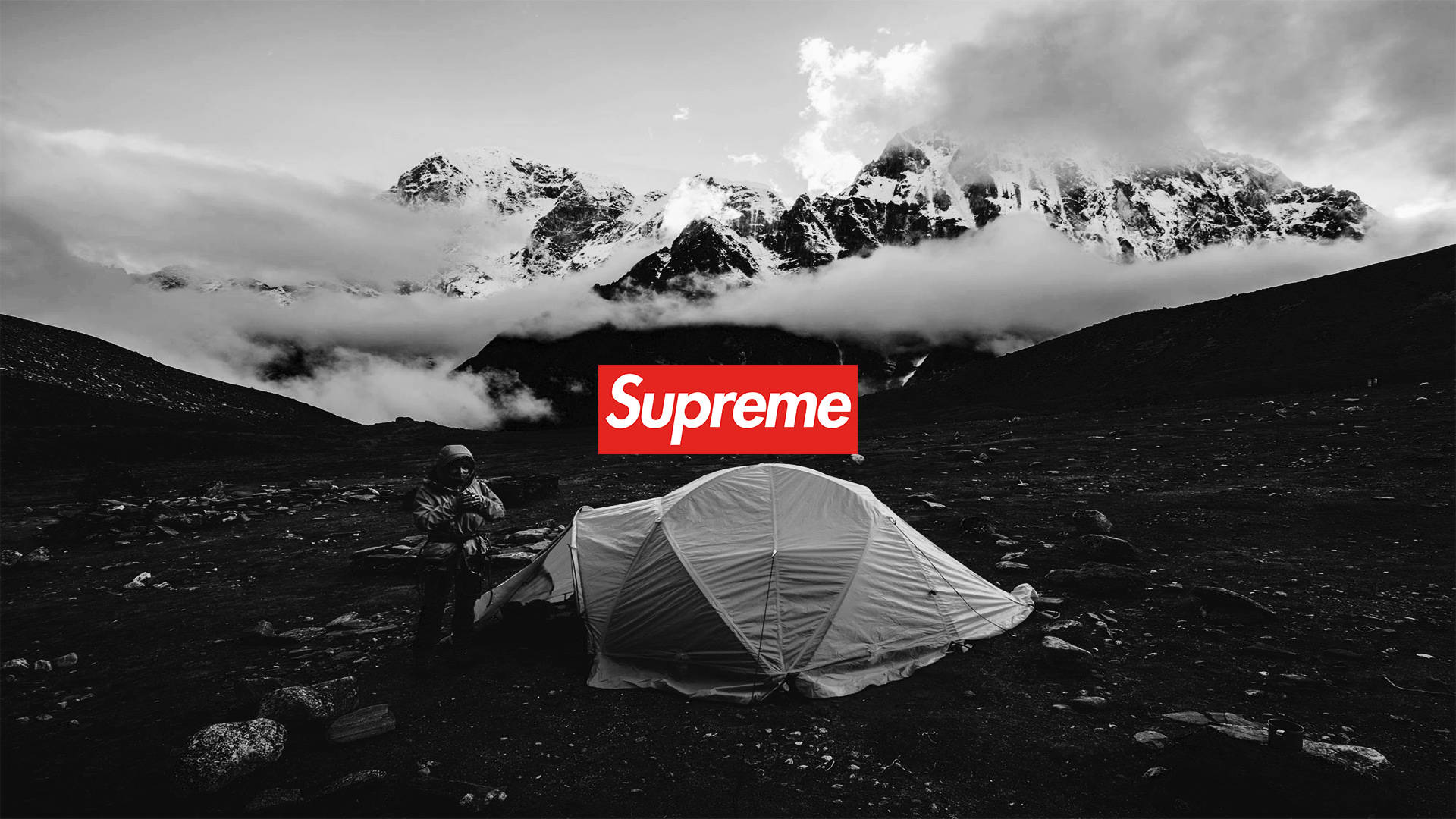 Cool Supreme 桌布 壁紙 — 一個孤獨的遠足者站在帳篷旁邊，在一個黑白分明的山谷中，有積雪的山峰和雲朵，下方是一個大膽的紅色Supreme標誌。