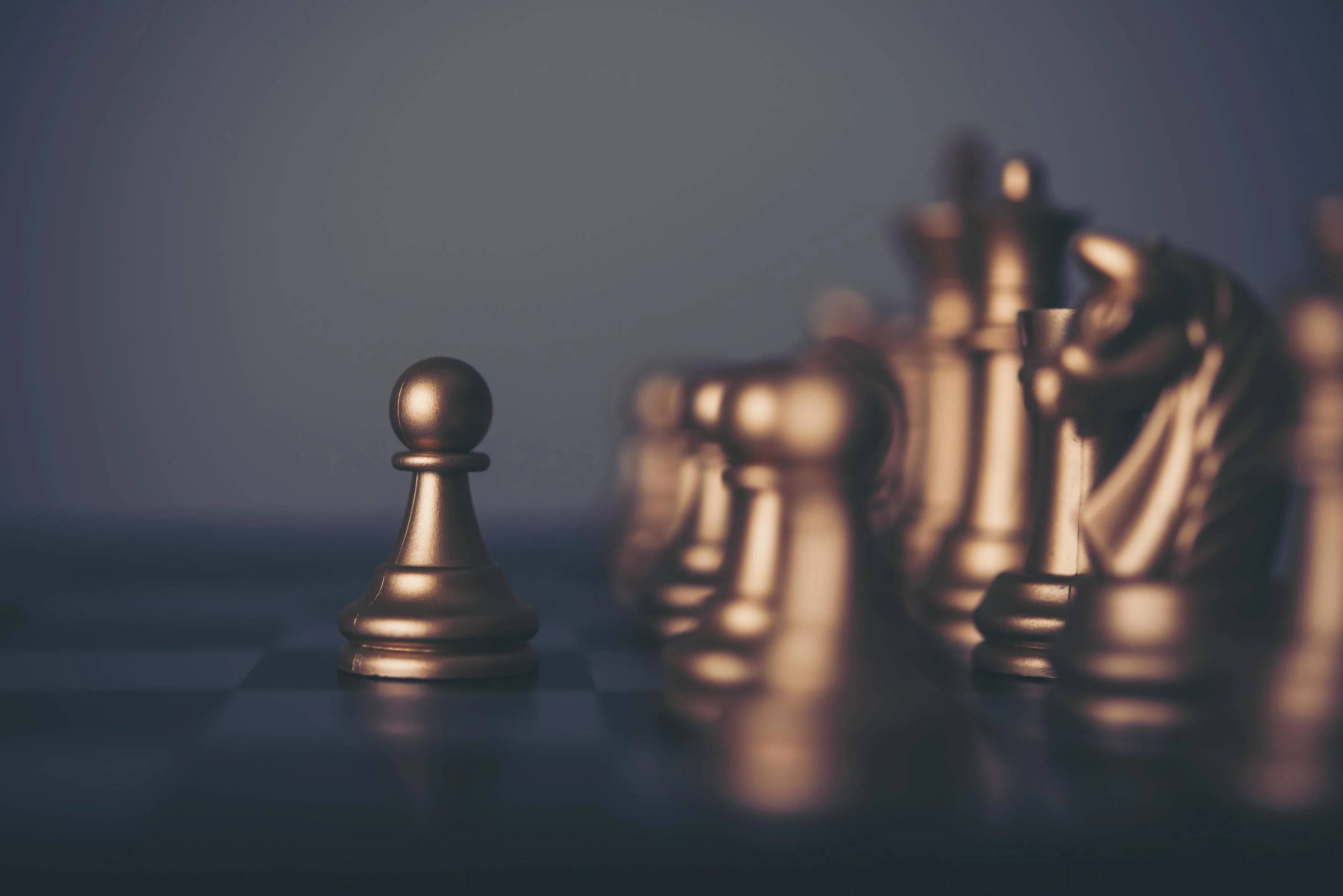 西洋棋 桌布 壁紙 — 一個孤獨的金色兵卒在棋盤上清晰對焦，而其他棋子則在柔和燈光下模糊成背景。