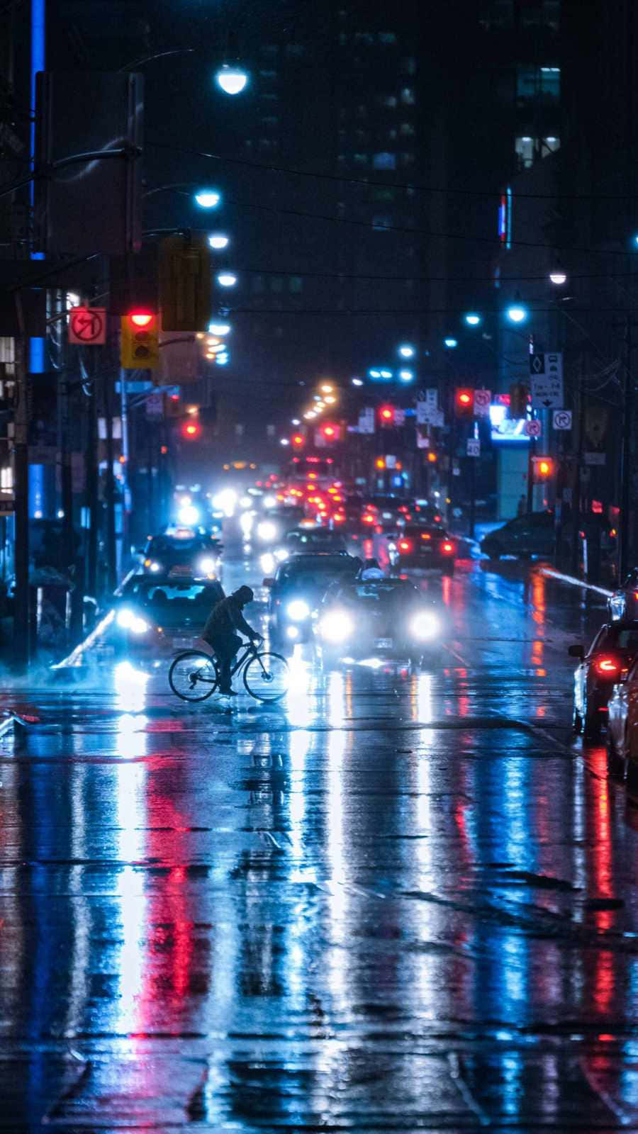 Road 桌布 壁紙 — 一個孤獨的騎自行車者在夜間穿過被雨水浸濕的城市街道，被汽車頭燈和路燈的鮮豔紅色和藍色反射照亮。