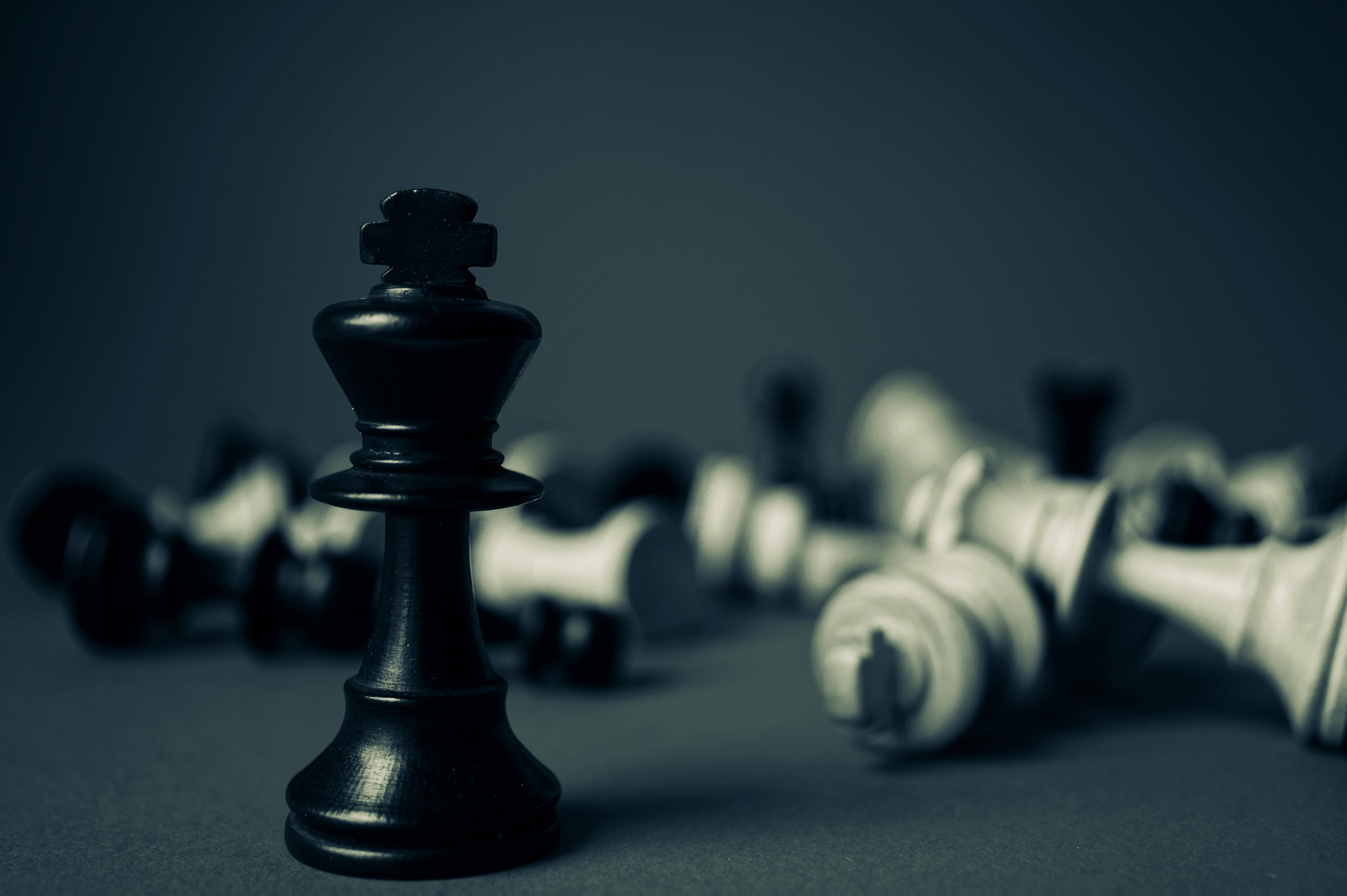 Screen 桌布 壁紙 — 一個孤獨的黑色國王棋子直立著，而倒下的白色棋子散落在模糊的背景中。