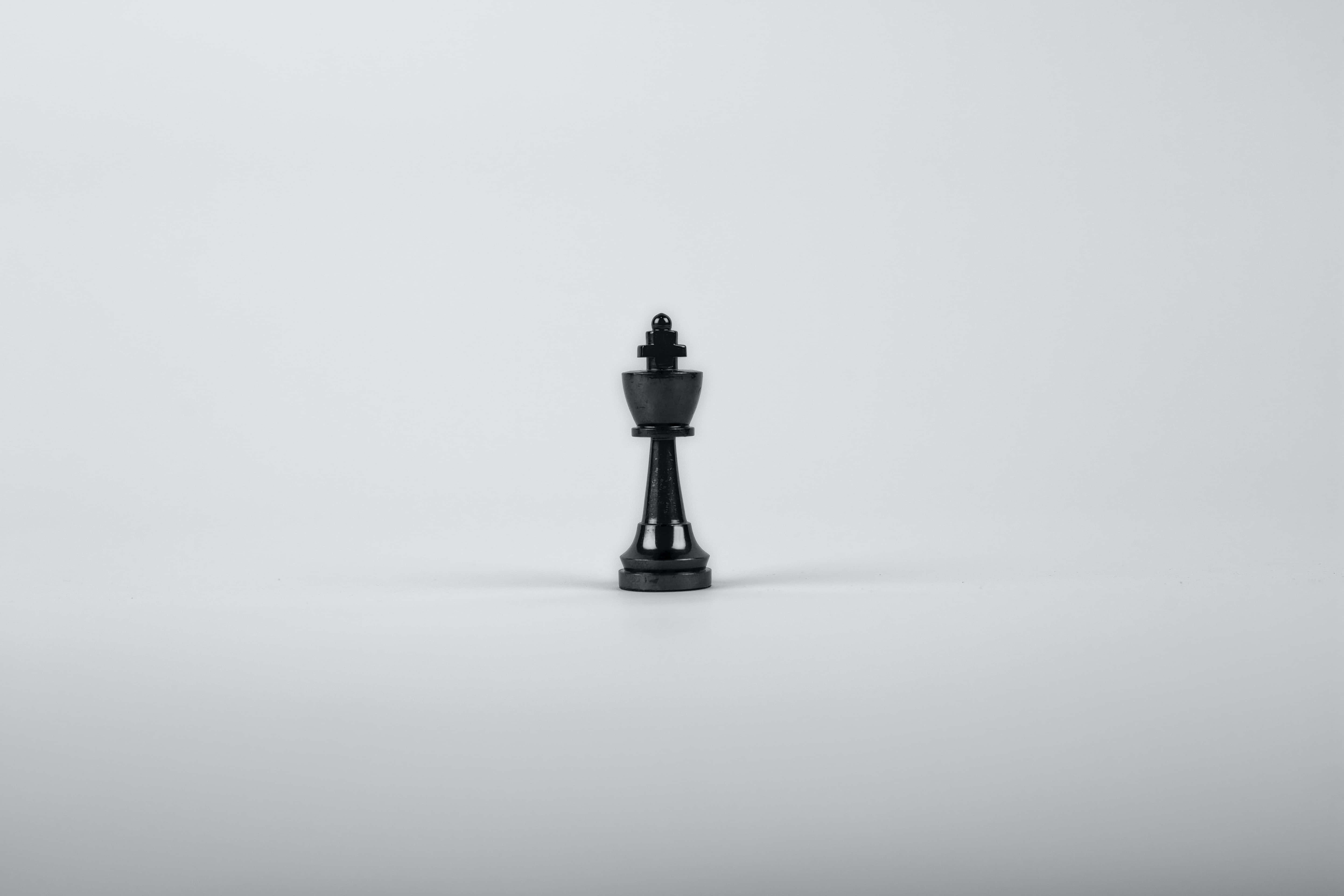黑白 桌布 壁紙 — 一個孤獨的黑色國王棋子置於白色表面中央，在柔和的工作室燈光下。