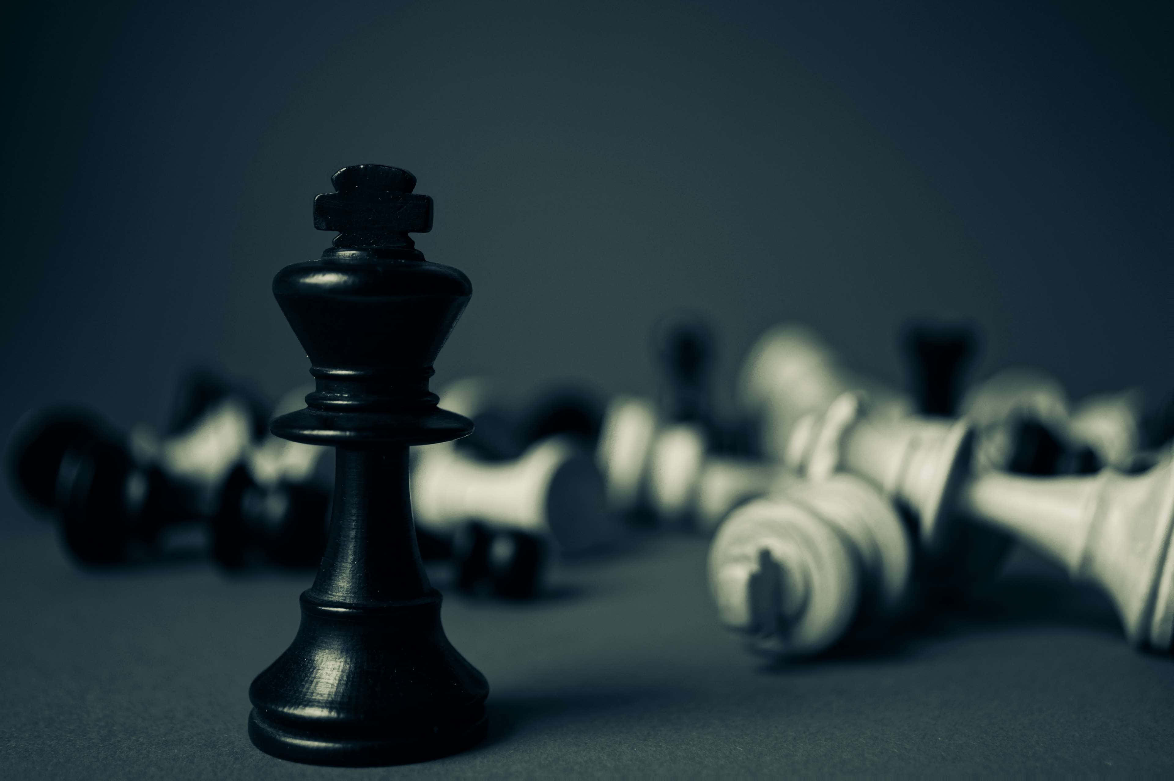 Black And White Chess 桌布 壁紙 — 一個孤獨的黑色西洋棋國王直立，而倒下的白色棋子散落在模糊的背景中。