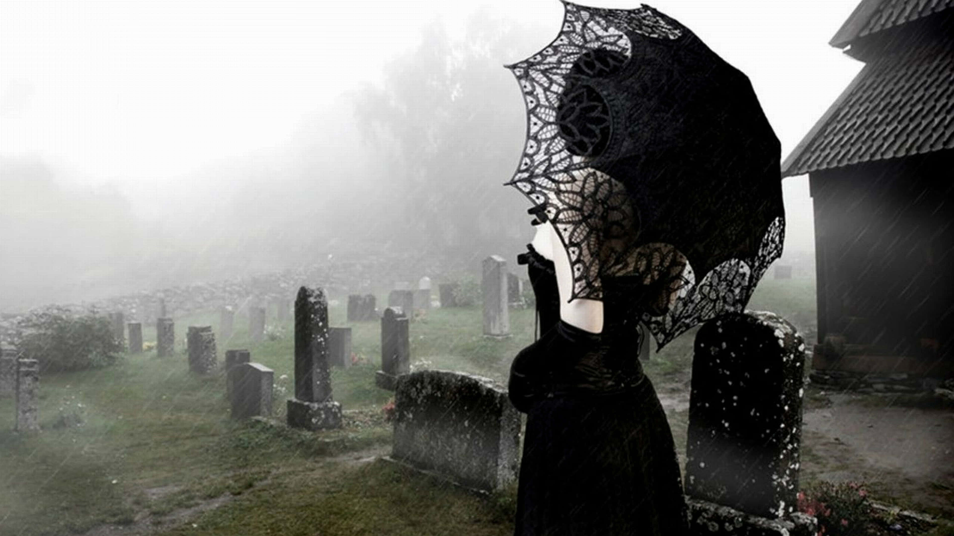 哥德式動圖 桌布 壁紙 — 一個孤獨的黑衣身影在霧雨濕透的墓地中，手持裝飾性蕾絲傘，周圍是風化的墓碑。