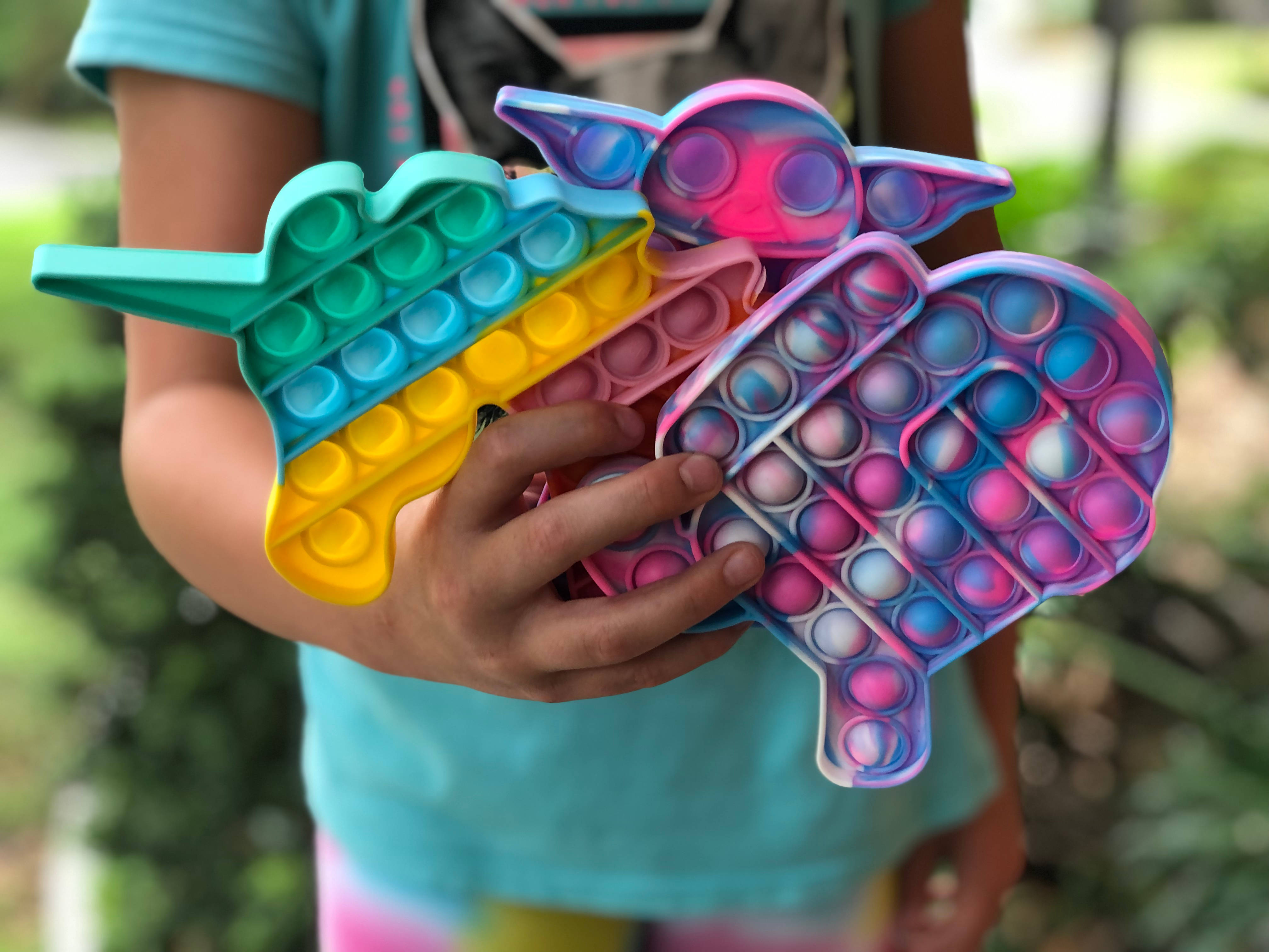 Fidget Toys 桌布 壁紙 — 一個孩子在戶外拿著三個色彩繽紛的彈力減壓玩具，形狀分別是獨角獸、尤達寶寶和心形。