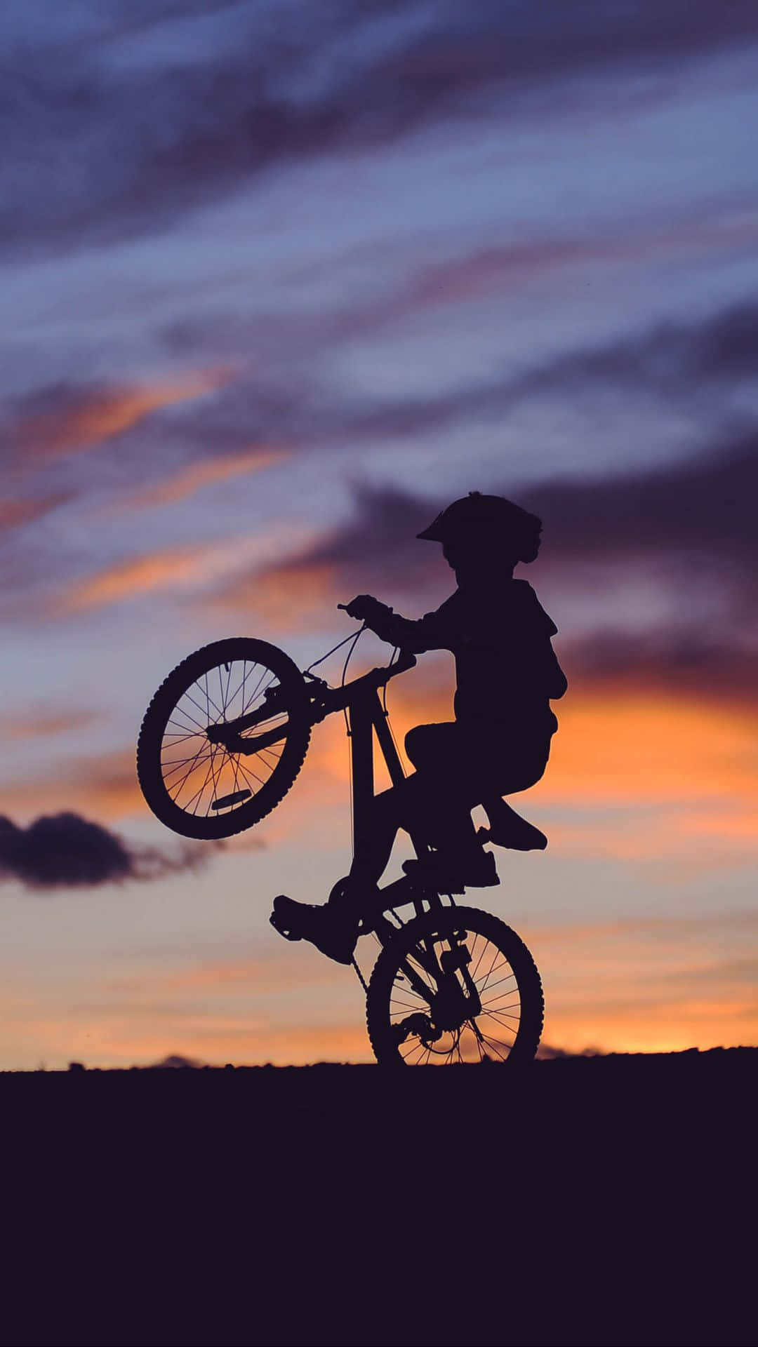 bmx 桌布 壁紙 — 一個孩子在腳踏車上做出翹孤輪動作的剪影，背景是充滿活力的黃昏天空，帶有橙色和紫色的雲彩。