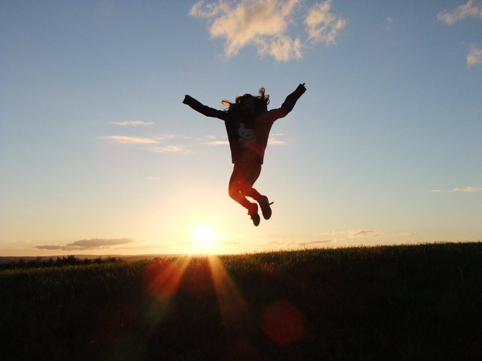 Jumping 桌布 壁紙 — 一個孩子在金色夕陽天空下歡樂地躍起，伴隨著鏡頭光暈和散落的雲朵。