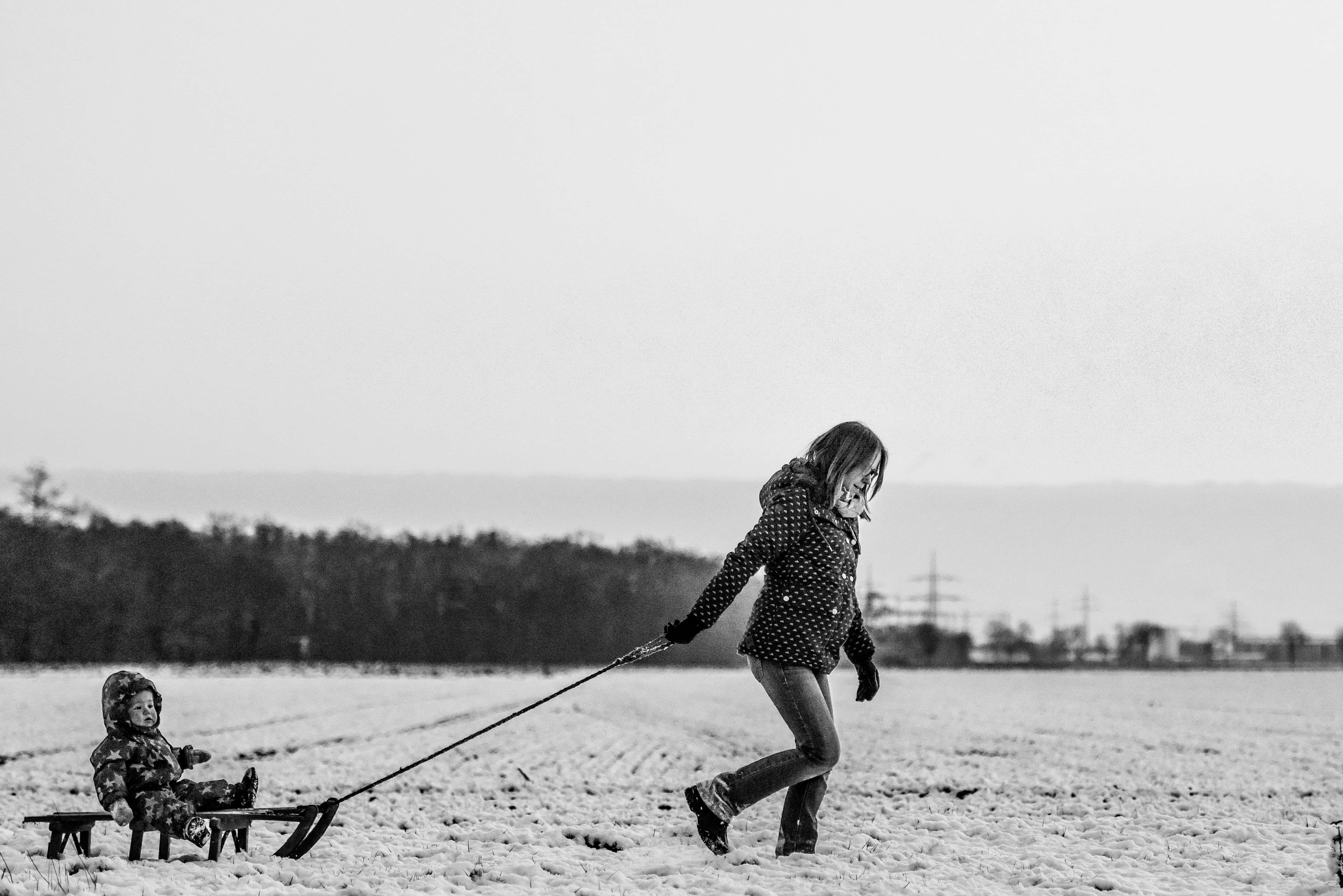 Mom 桌布 壁紙 — 一個孩子在陰天的雪地上拖著一個載有幼兒的雪橇。