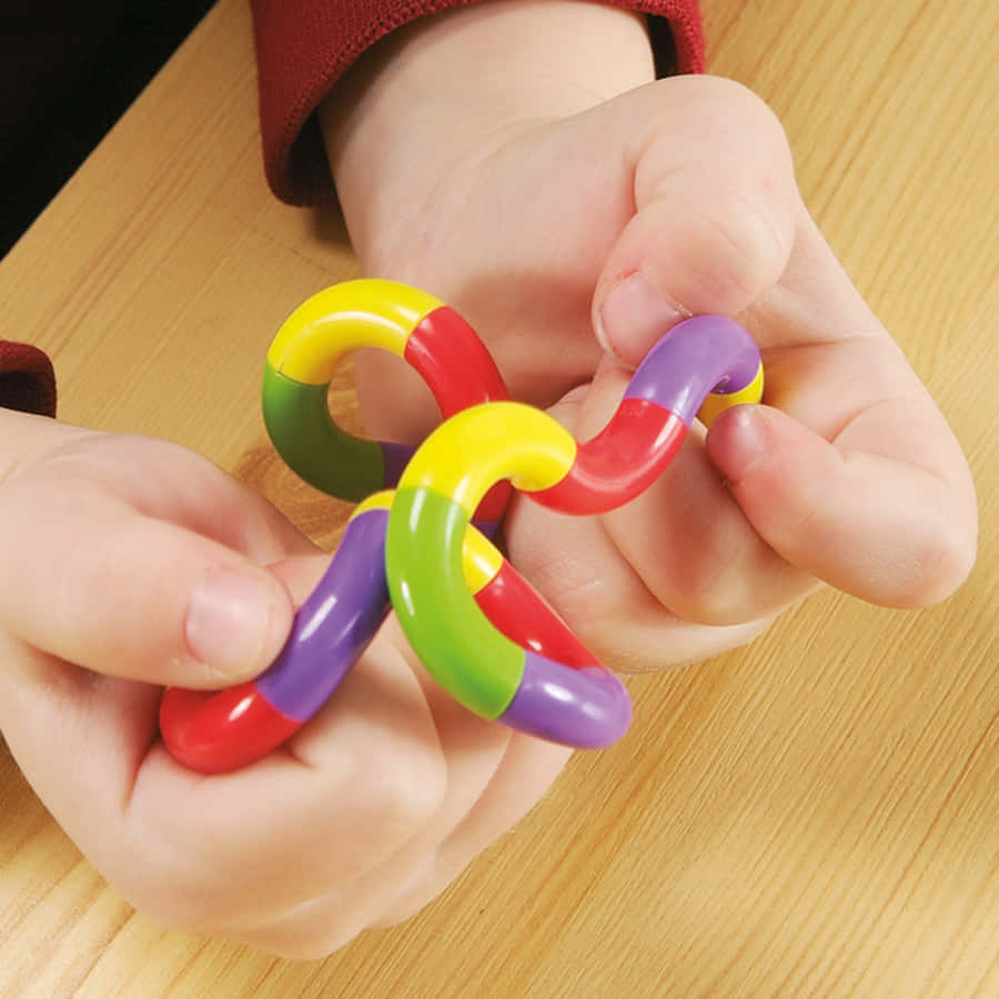Fidget 桌布 壁紙 — 一個孩子的手輕輕地拿著一個彩色磁力玩具鏈條在木桌上。