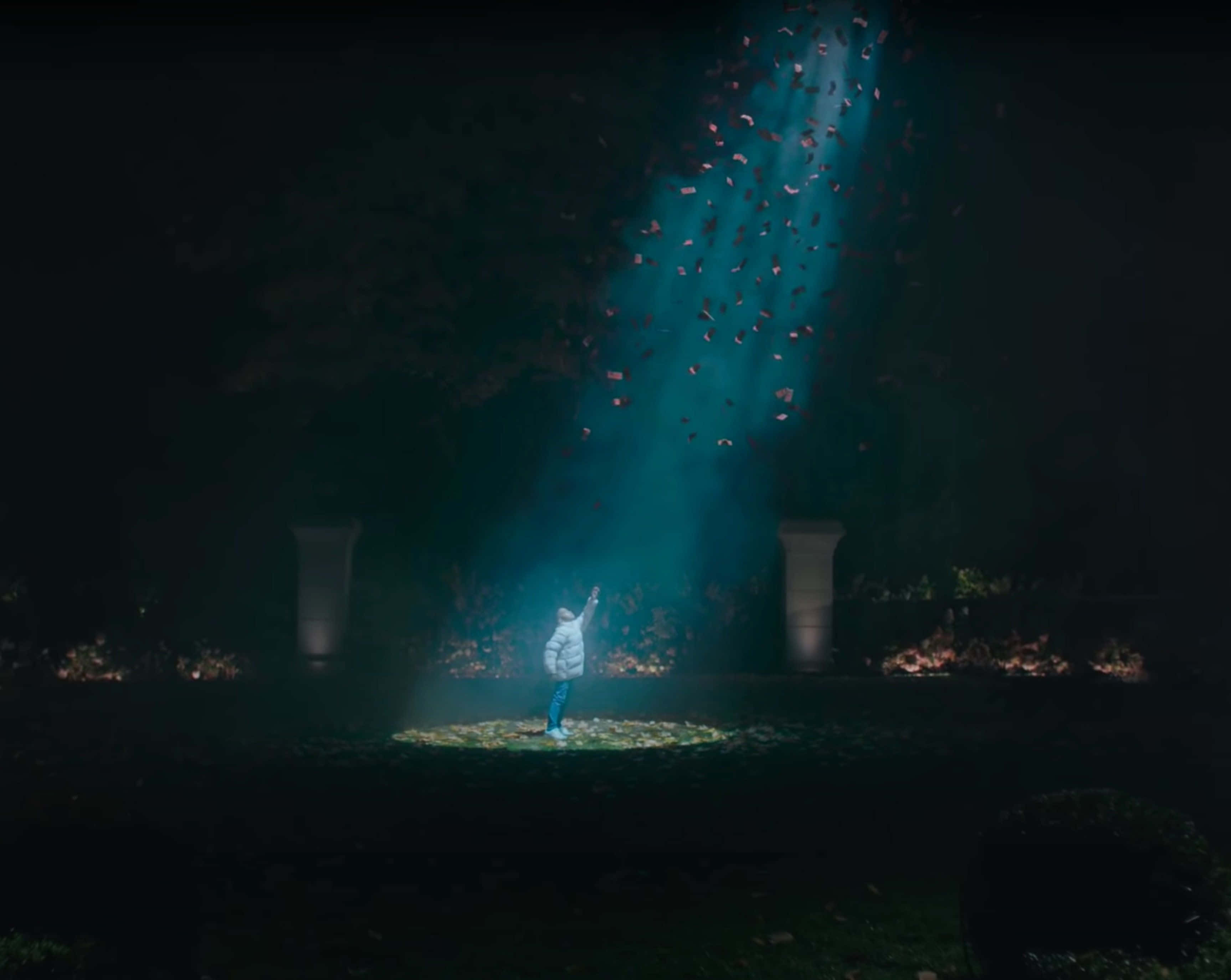 Drake 桌布 壁紙 — 一個孩子站在黑暗的花園中向上伸手，青綠色的光束照亮了他們周圍飄落的紅葉。
