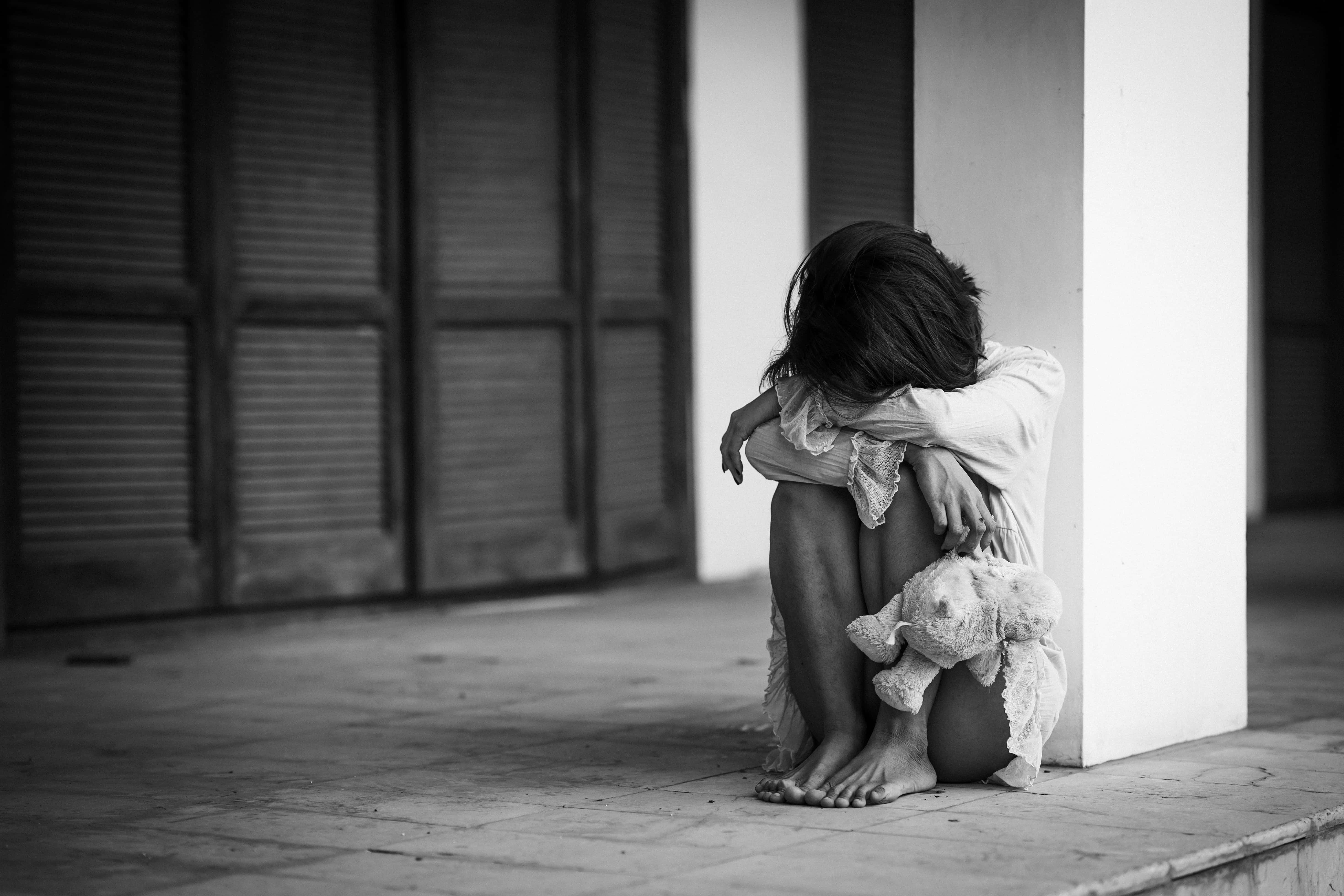 Depressed 桌布 壁紙 — 一個孩子蜷縮在瓷磚地板上靠著柱子，緊抓著一隻破舊的泰迪熊，畫面呈鮮明的黑白對比。
