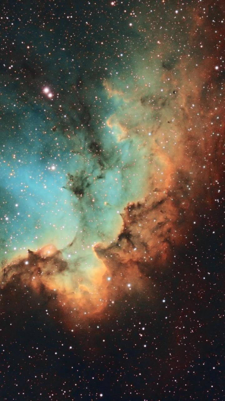 銀河 桌布 壁紙 — 一個宇宙星雲在充滿恆星的背景下，以鮮豔的青綠色和橙色旋轉，並帶有黑暗的宇宙塵埃帶。