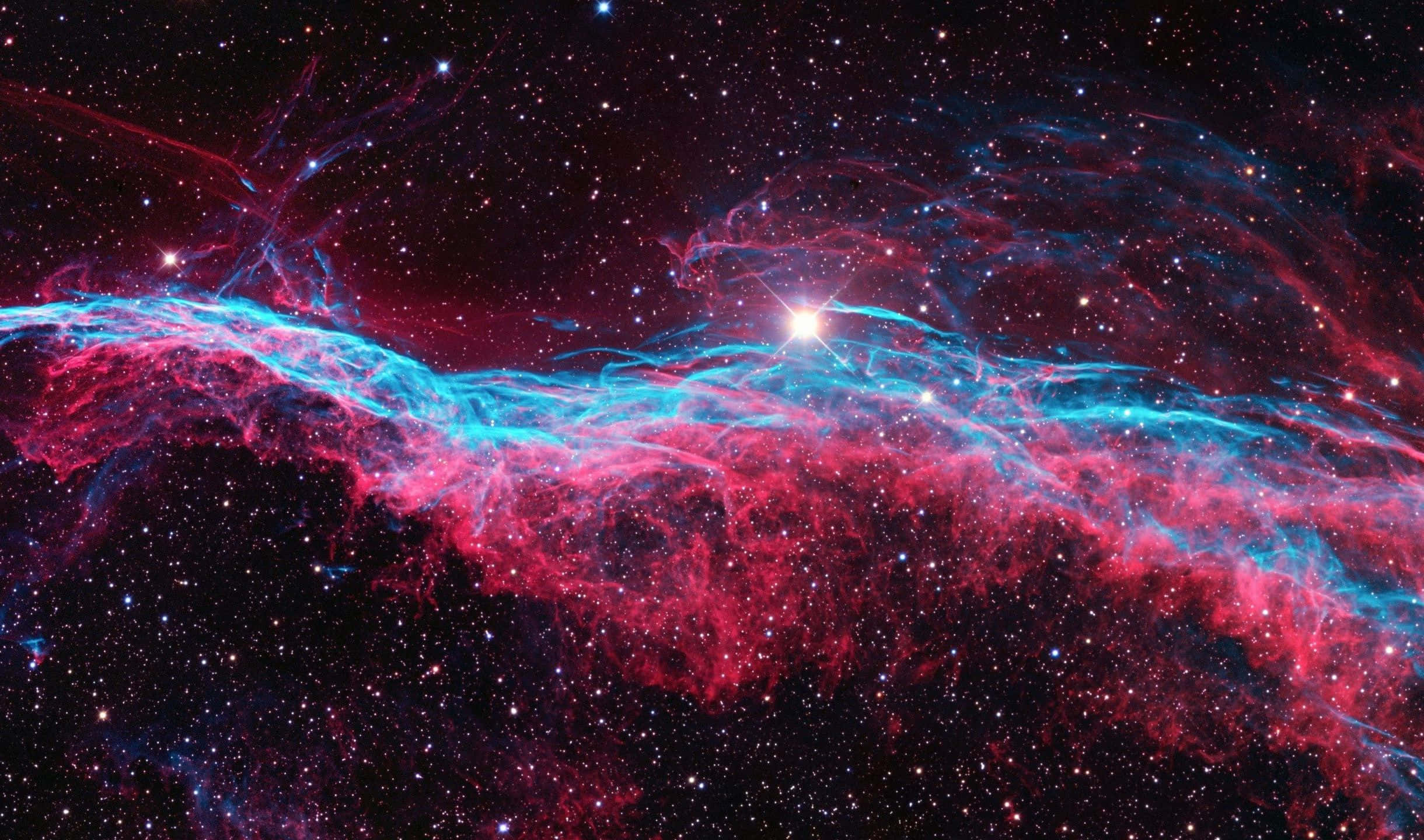 2440x1440 桌布 壁紙 — 一個宇宙星雲在星空中以鮮豔的紅色和電光藍色旋轉，一顆明亮的中心恆星照亮了宇宙塵埃。