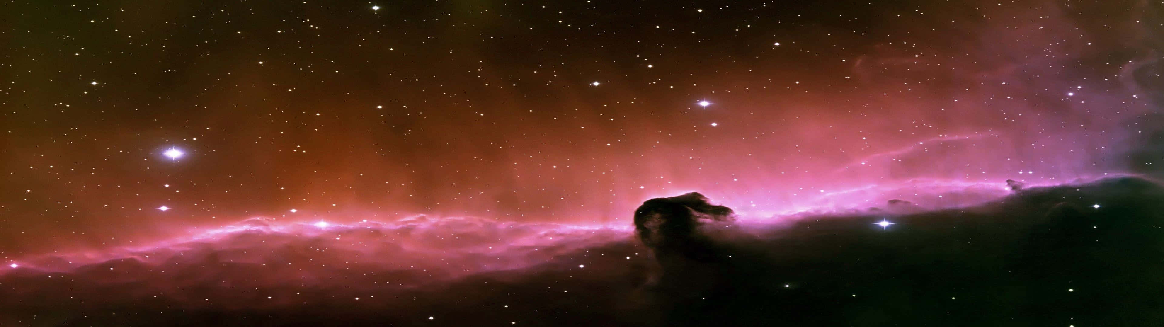 桌布 壁紙 — 一個宇宙星雲在星空中發出鮮豔的粉紅色和橙色光芒，並帶有天體形成的黑暗剪影。