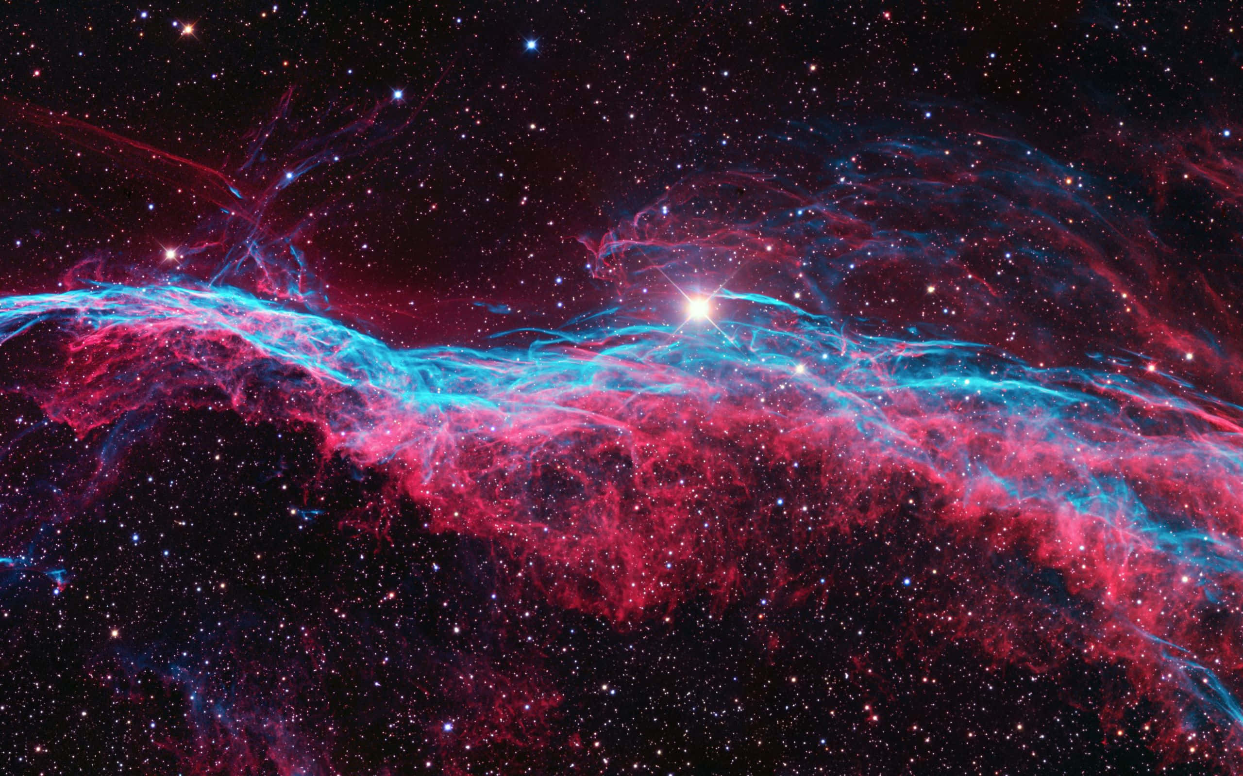 酷炫太空 桌布 壁紙 — 一個宇宙星雲在星空背景下以鮮豔的紅色和電光藍色旋轉，明亮的中央恆星照亮了宇宙塵埃。